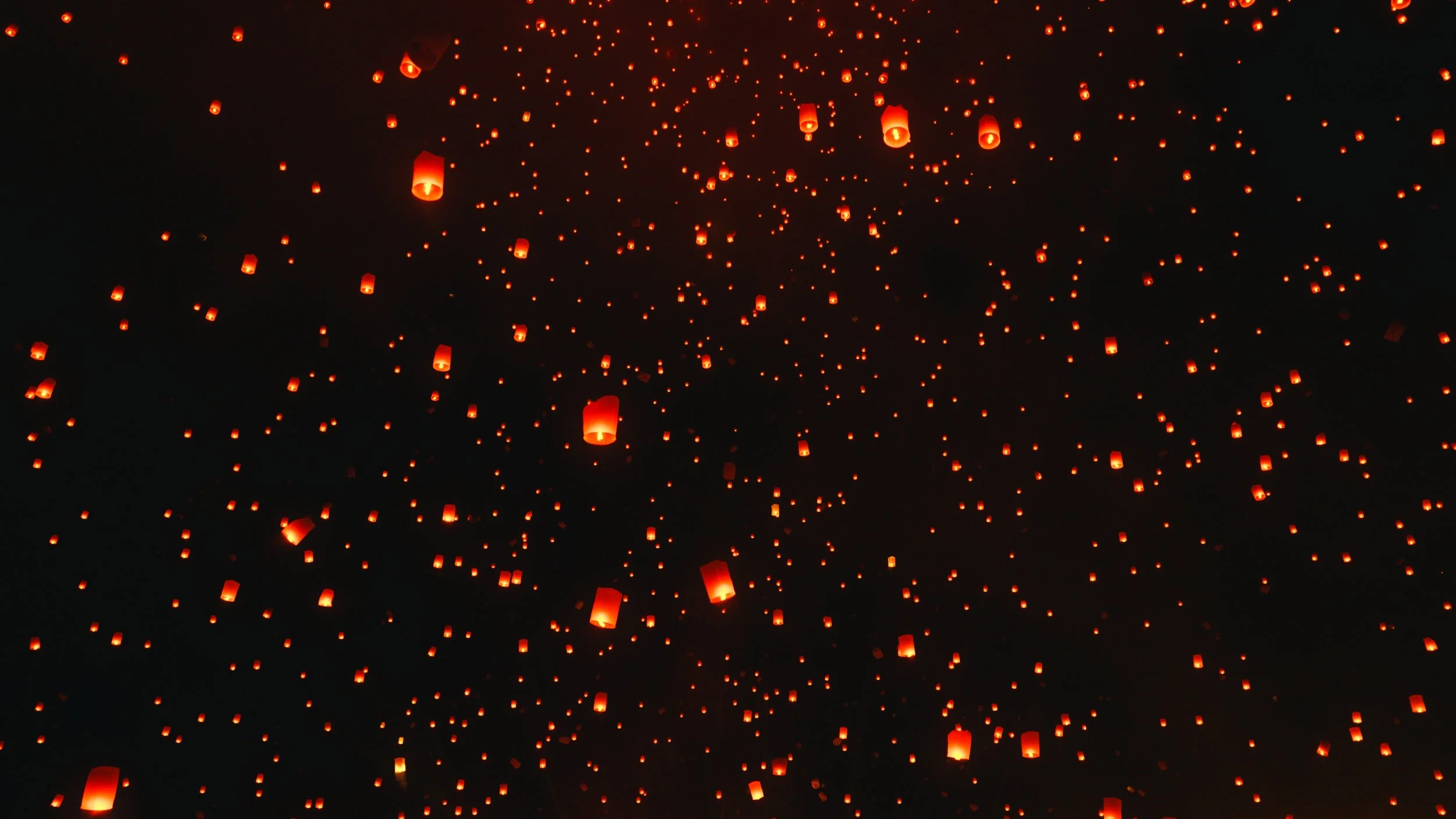 Miles de linternas de papel de color naranja flotando en la noche después de ser liberadas al aire.