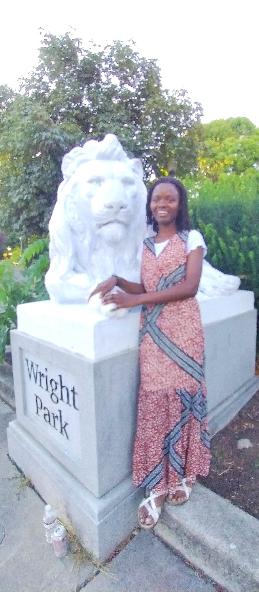 A woman standing next to a white marble lion statue at Wright Park, smiling with her arm resting on the statue in an outdoor setting with greenery.