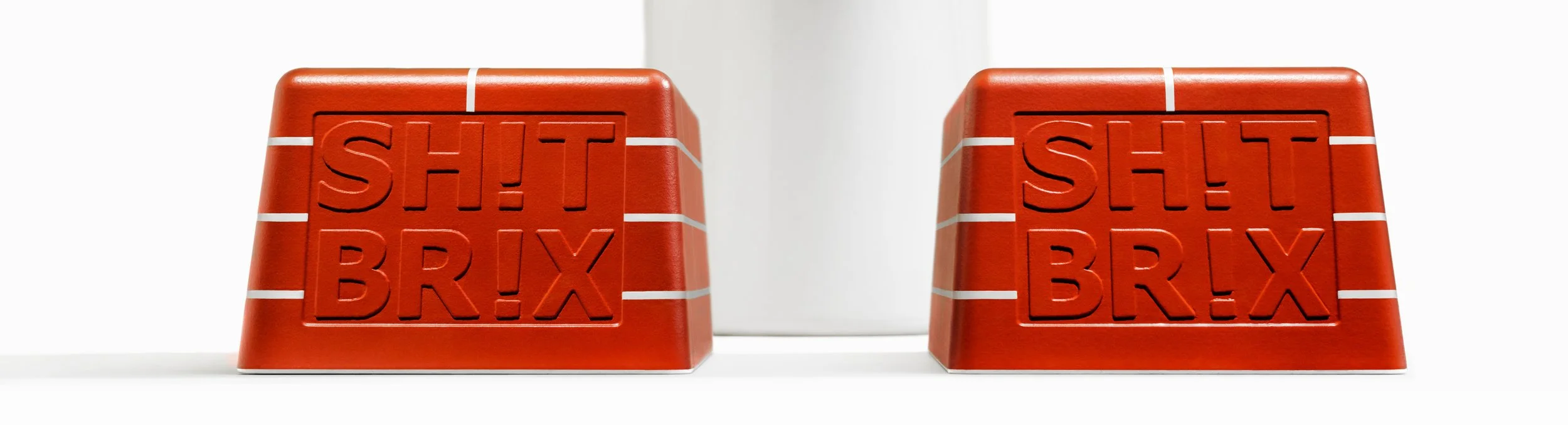 Two red blocks with the words "SH!T BR!X" embossed on them, with white lines on a white surface against a white background.