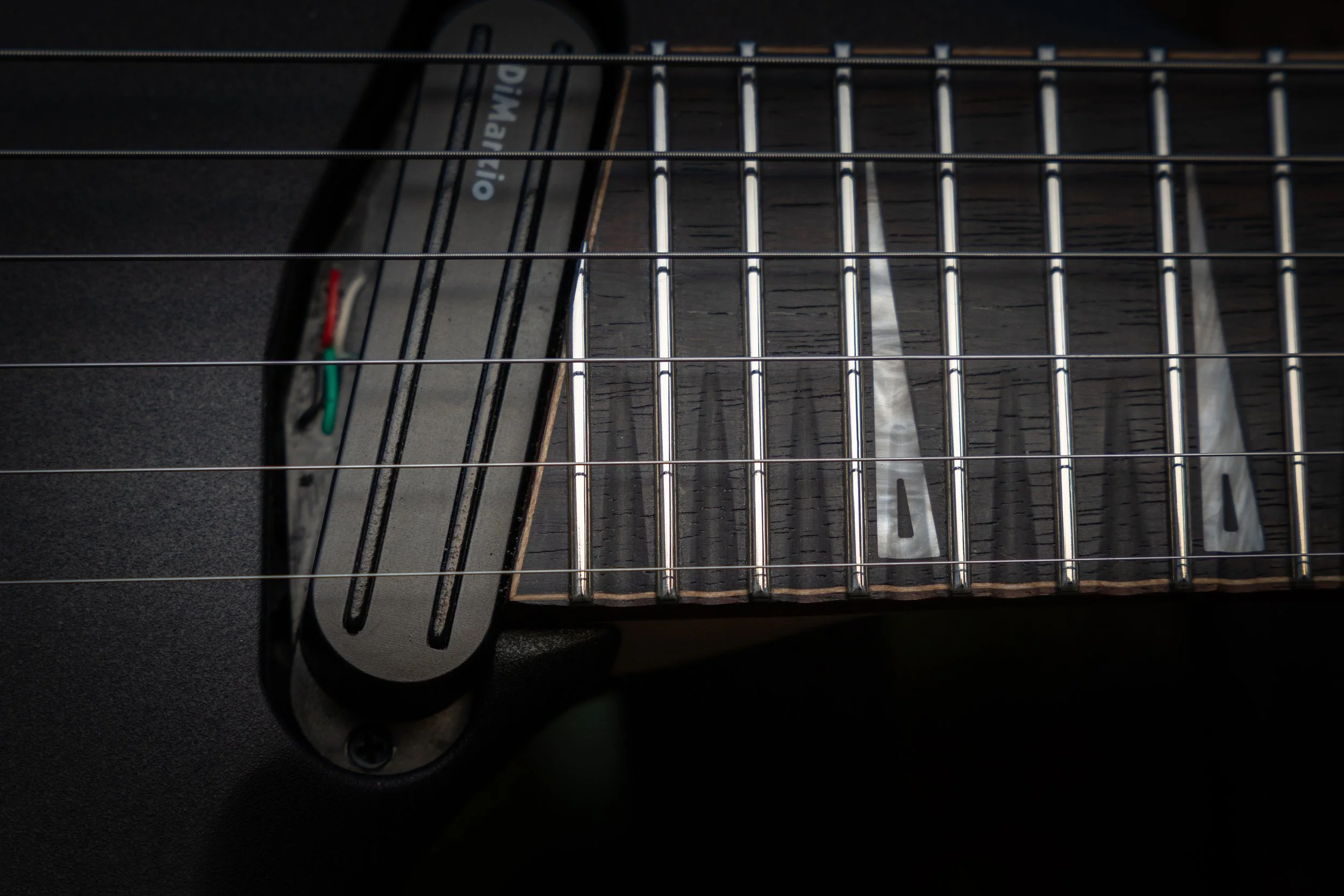 Close-up of electric guitar strings and fretboard, showing a portion of the guitar body and neck.