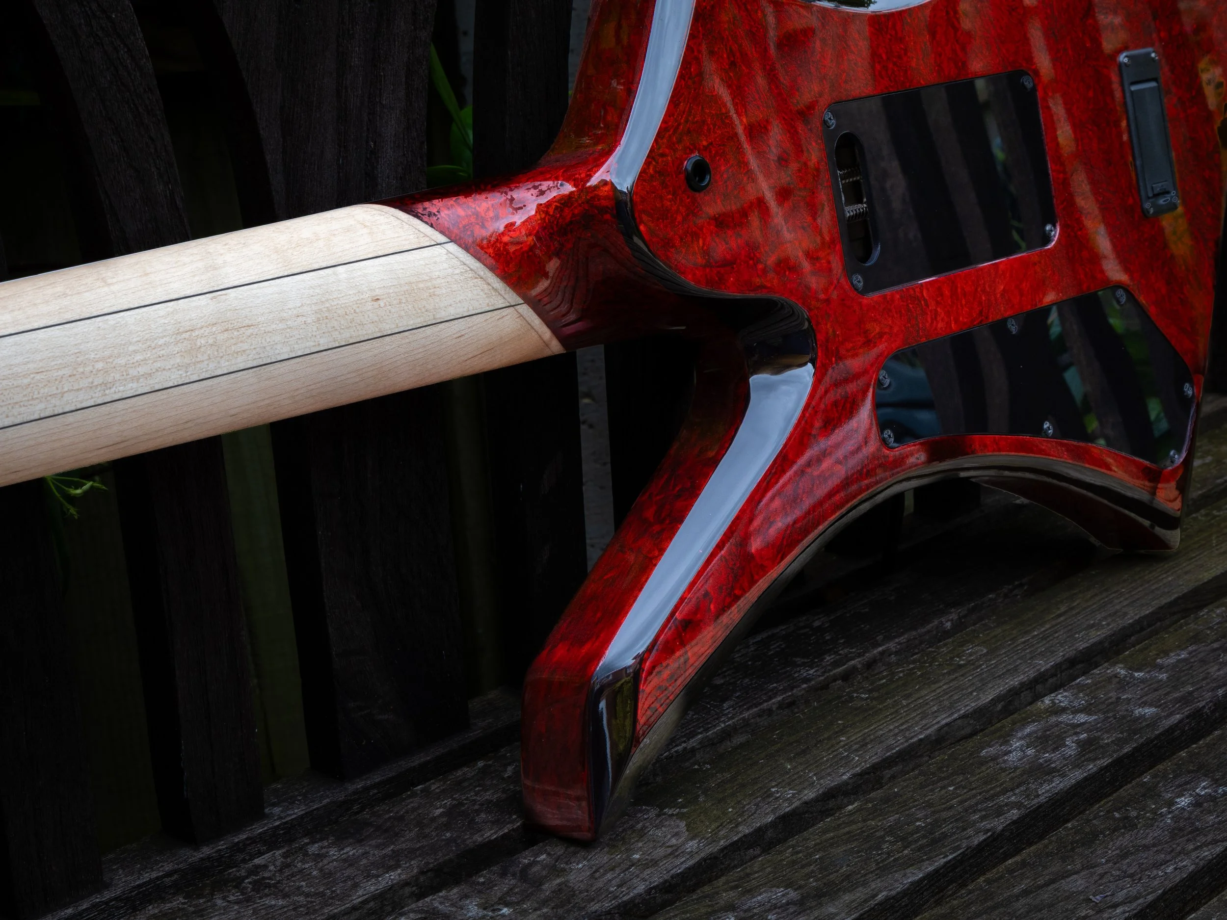Close-up of the back of an electric guitar with a red wood grain finish, showing the neck joint, some electronic parts, and the guitar's body against a dark wooden background.