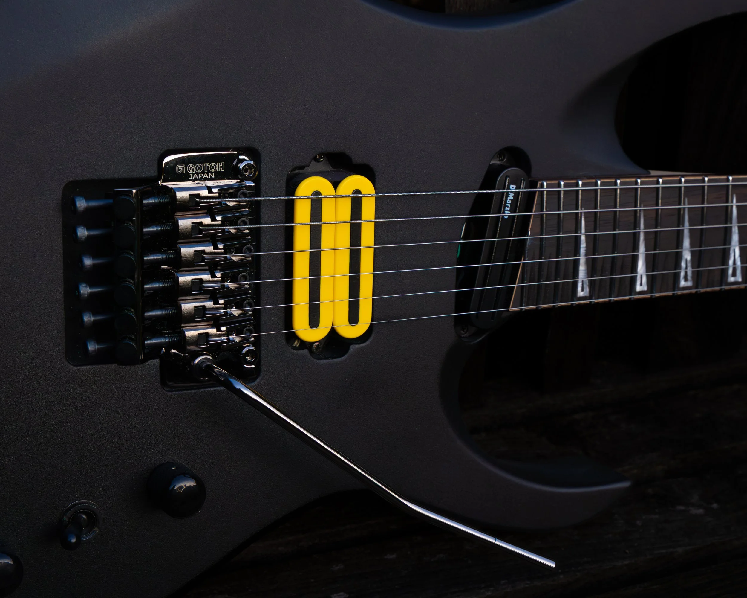 Close-up of a black electric guitar with yellow numbered speed bumps, mechanical bridge, and metal strings.