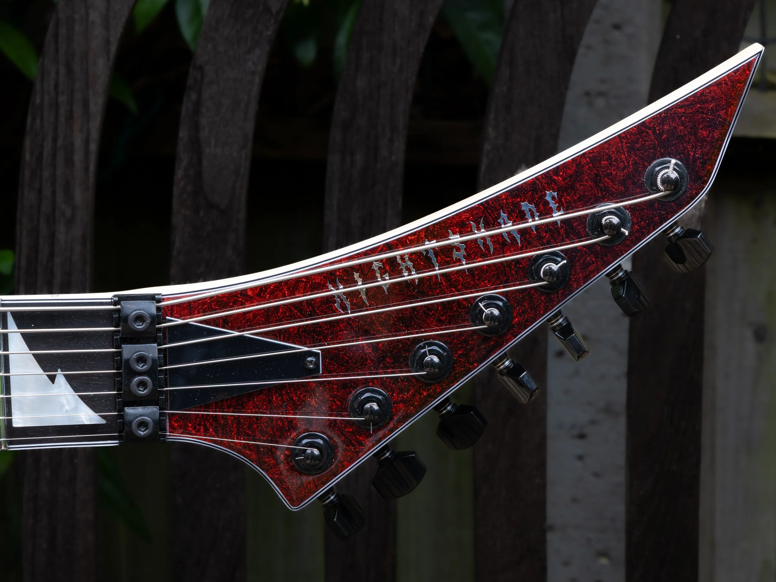 Close-up of the headstock of an electric guitar with a red and black marbled design, tuning pegs, and strings.