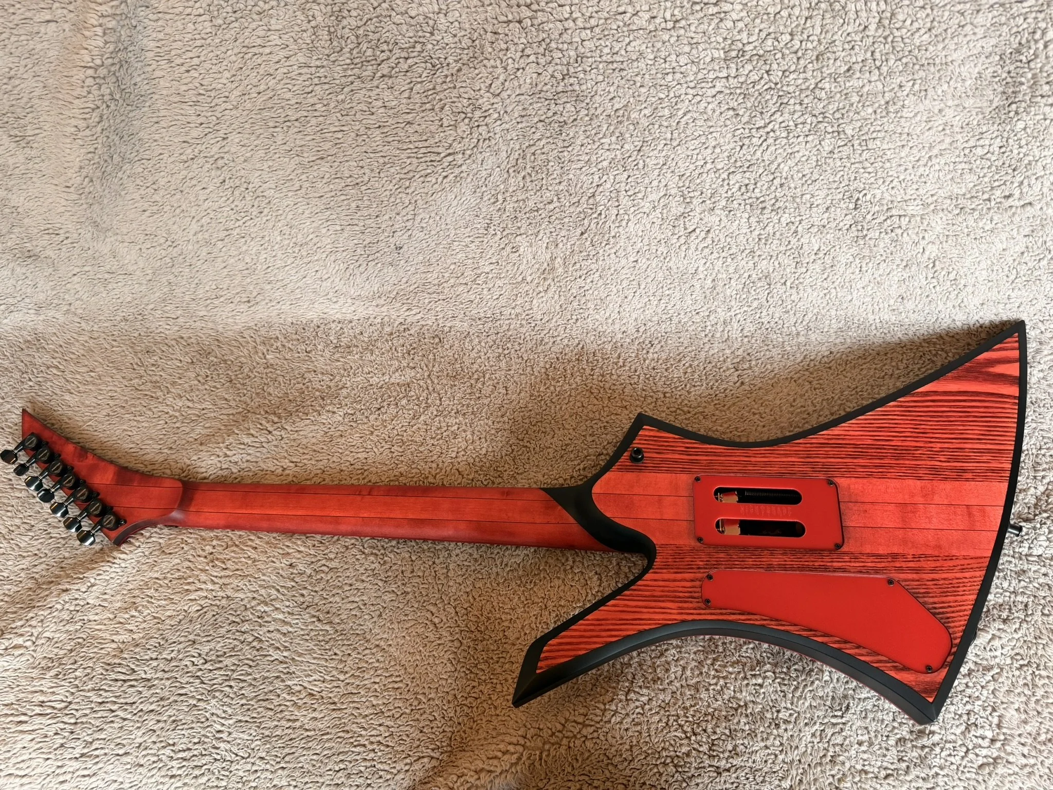 A red and black electric guitar with a wooden finish is placed on a beige carpet.