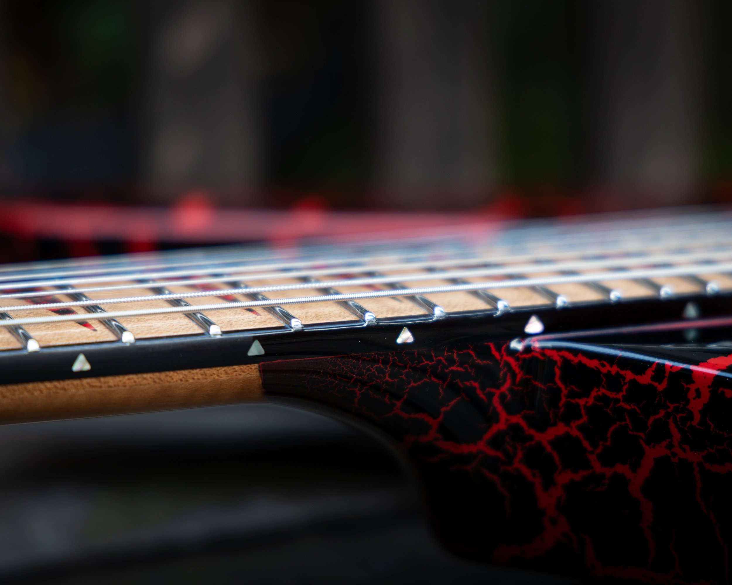 Close-up of a guitar fretboard with metal frets and red LED lights underneath, showing red lightning pattern on the body.
