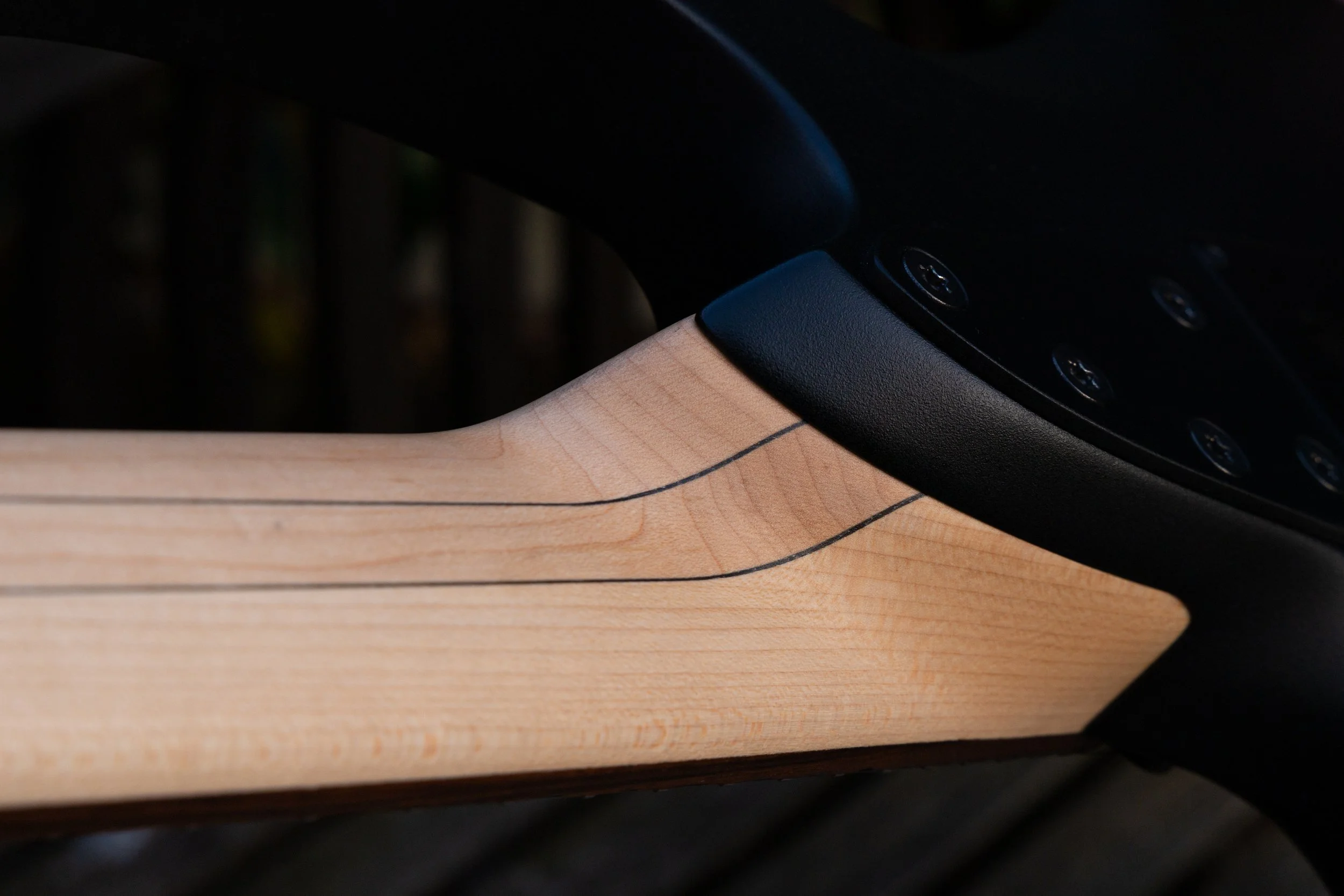 Close-up of a wooden musical instrument, possibly a guitar, with visible fret markings and a body made of light-colored wood.