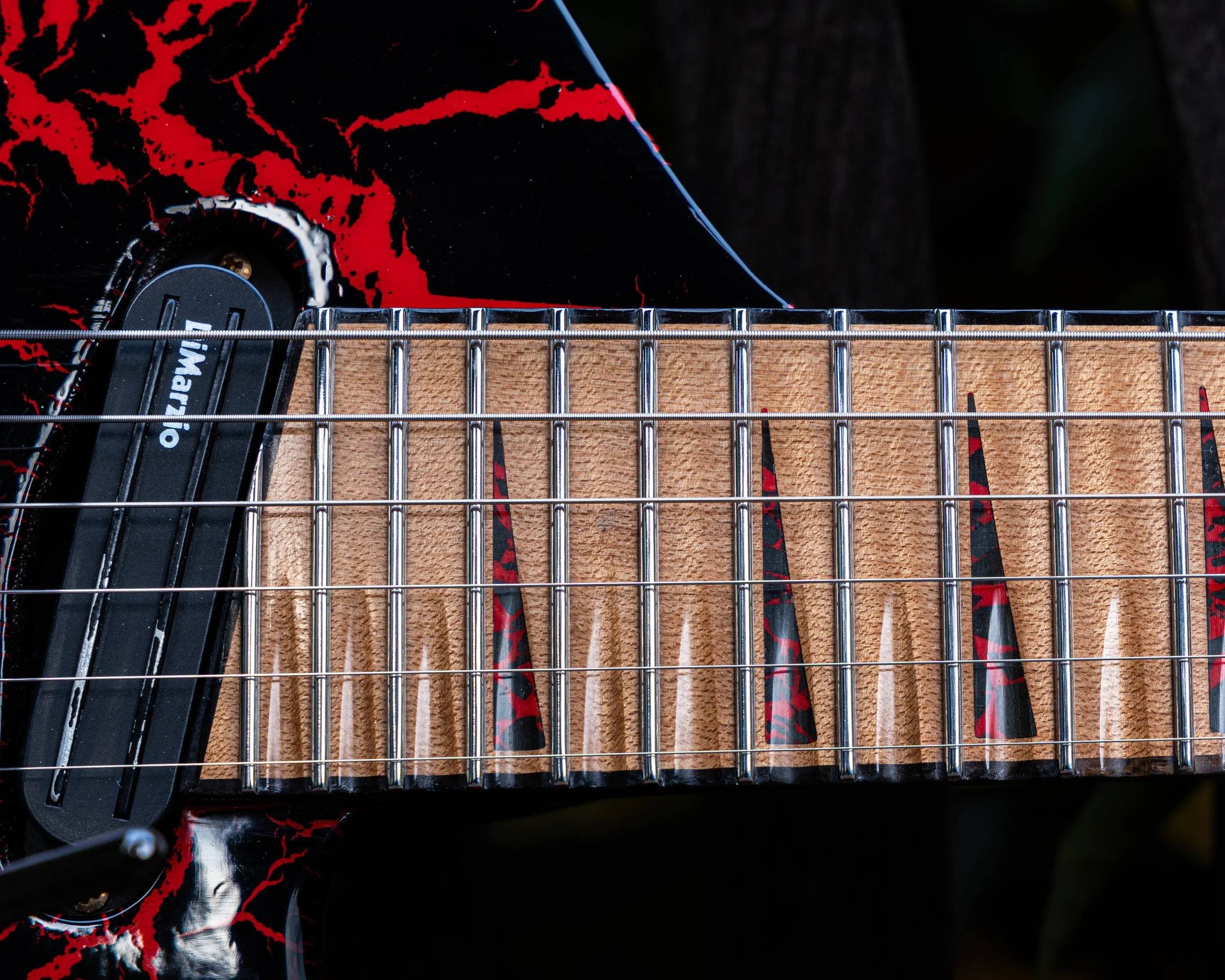 Close-up of a guitar's bridge and strings, with the guitar body featuring black and red cracked paint design.
