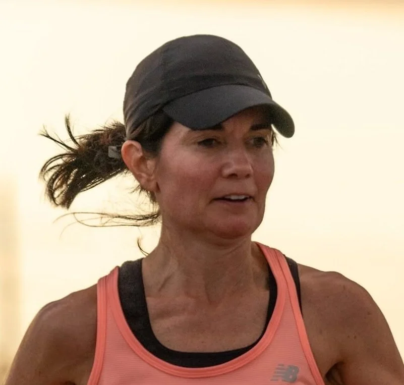 A woman wearing a black cap and a pink tank top, possibly running or exercising indoors.