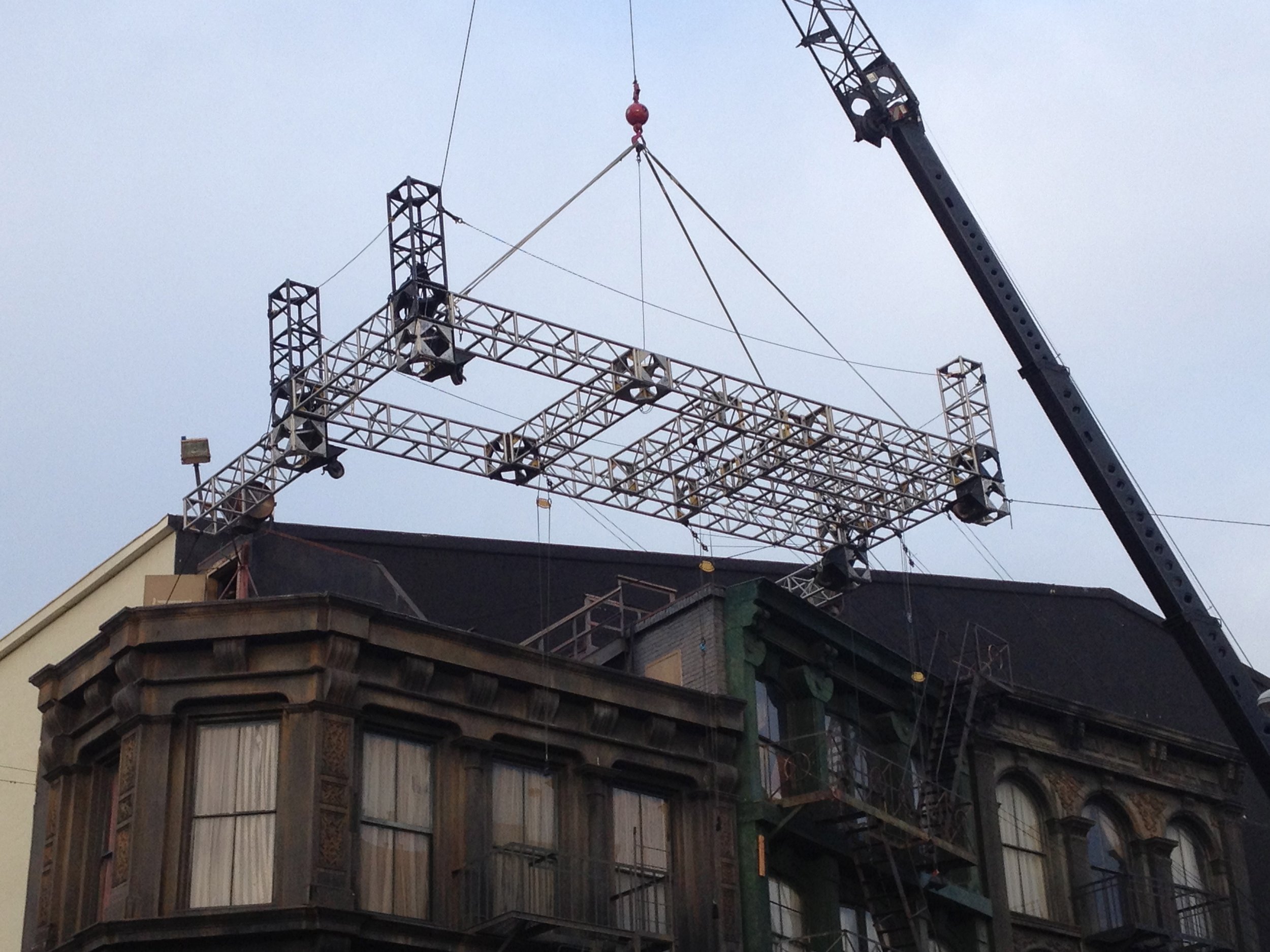 A construction crane lifting materials on top of a multi-story building under construction with several workers visible at the site.