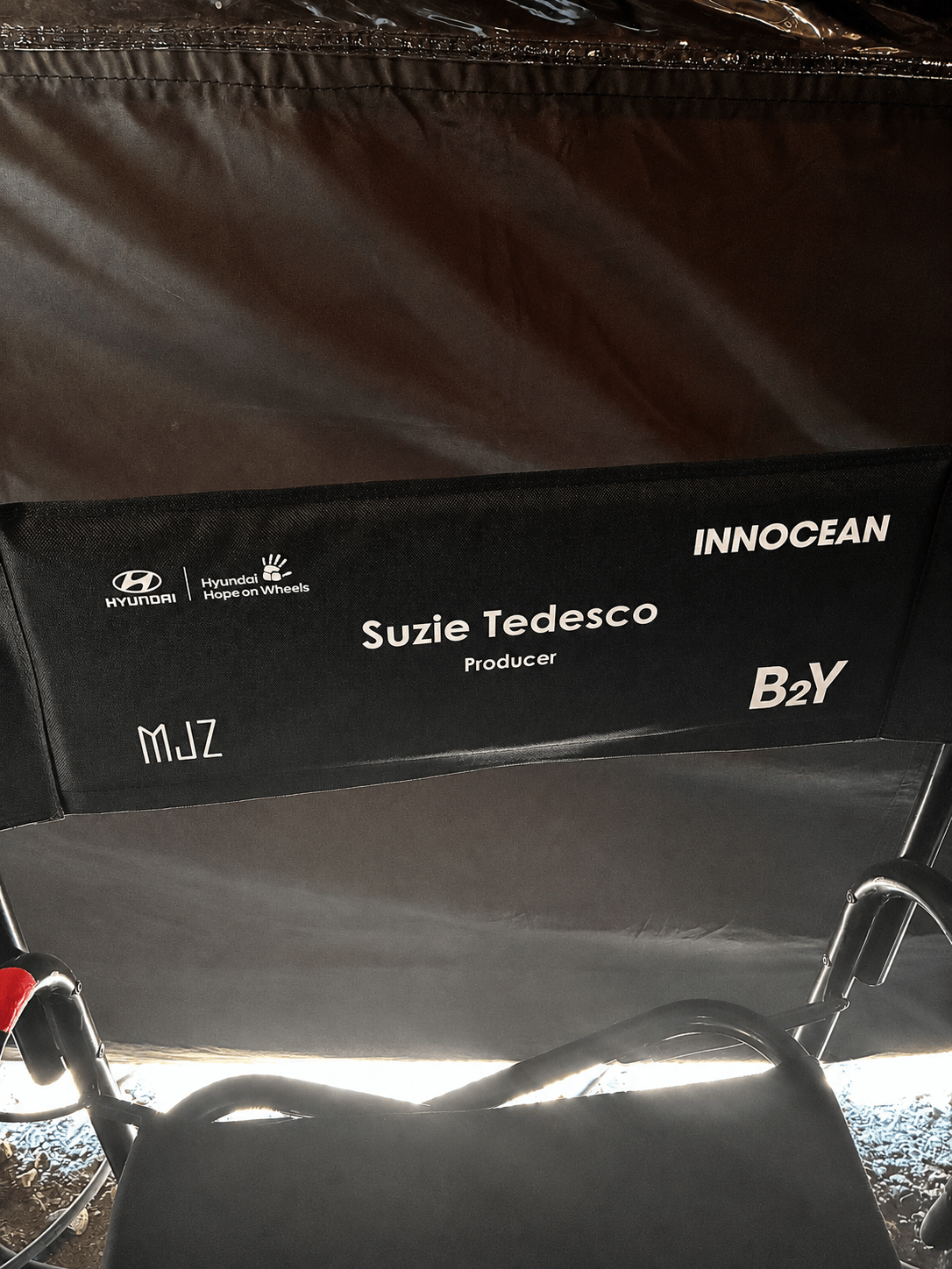 Name tag on the back of a seat with the name Suzie Tedesco, producer, and various company logos including Hyundai, Innocan, M.JZ, and B2Y.