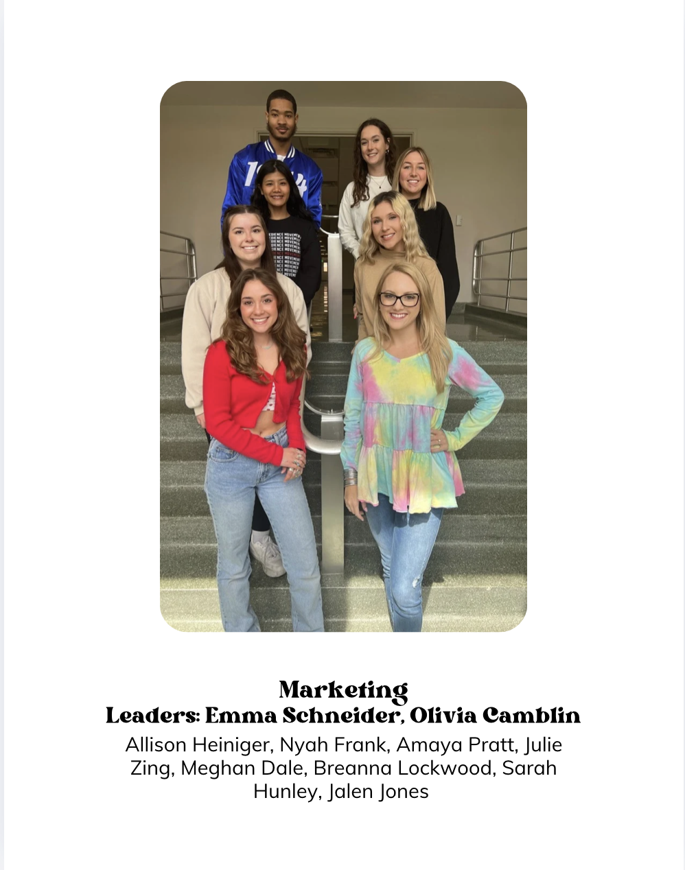 A group of eight young women and one young man posing on a staircase inside a building. The group appears to be diverse in ethnicity and is casually dressed. The photo is part of a presentation slide titled "Marketing," with leadership names listed b