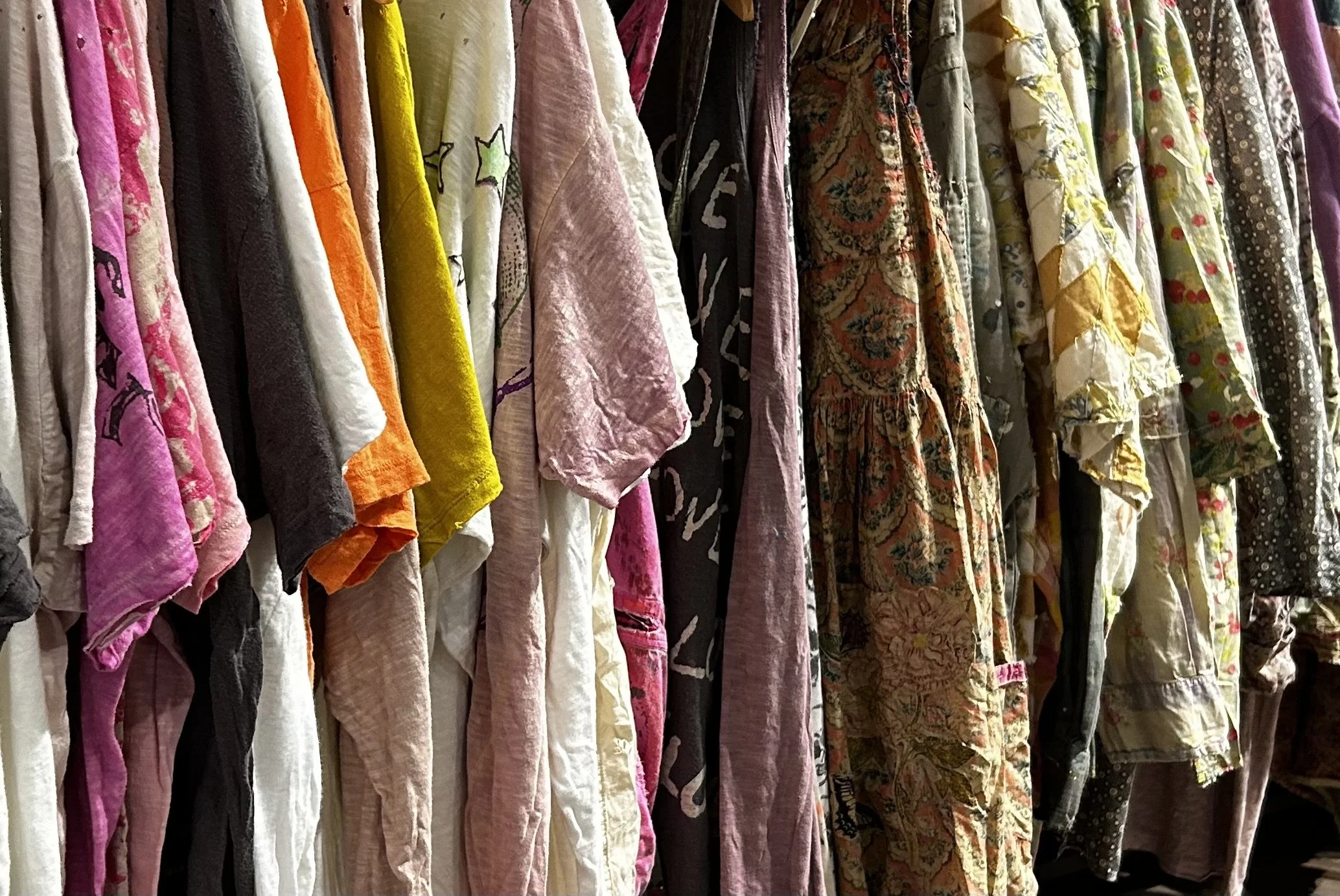 Various colorful and patterned fabric pieces hanging side by side on a rack.