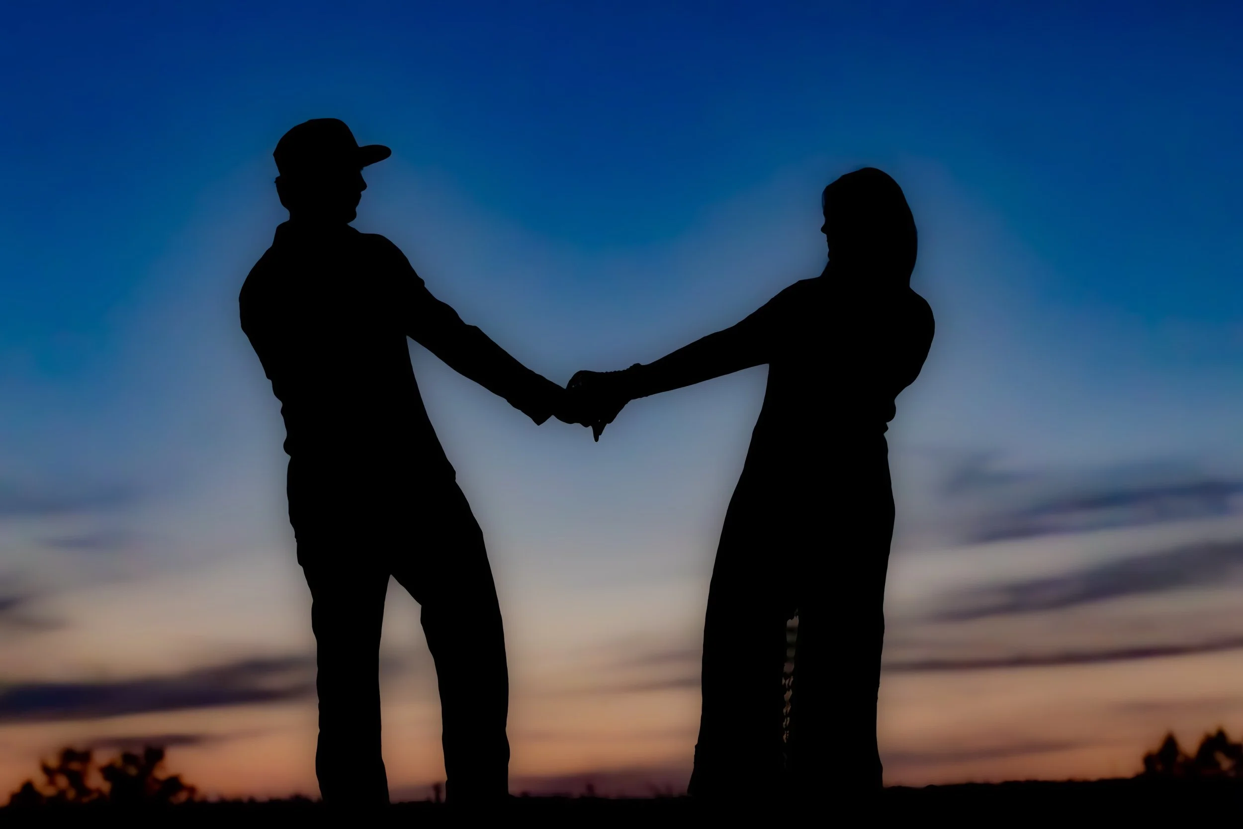 Silhouette of two people holding hands against a colorful sunset sky.
