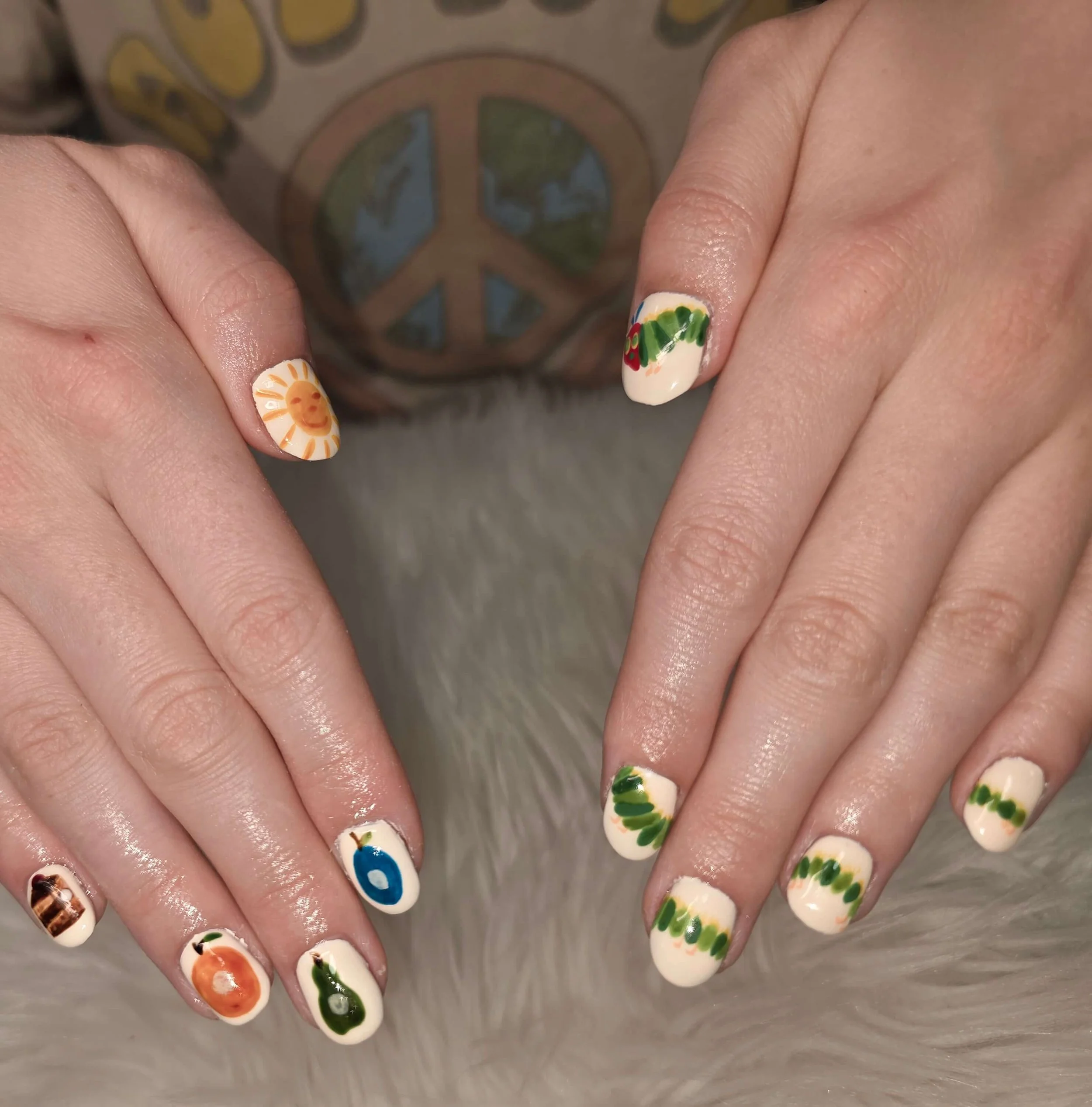Close-up of hands showing decorated nails with colorful and sunny graphic designs, including a sun, a rainbow, a wintry scene, and greenery.