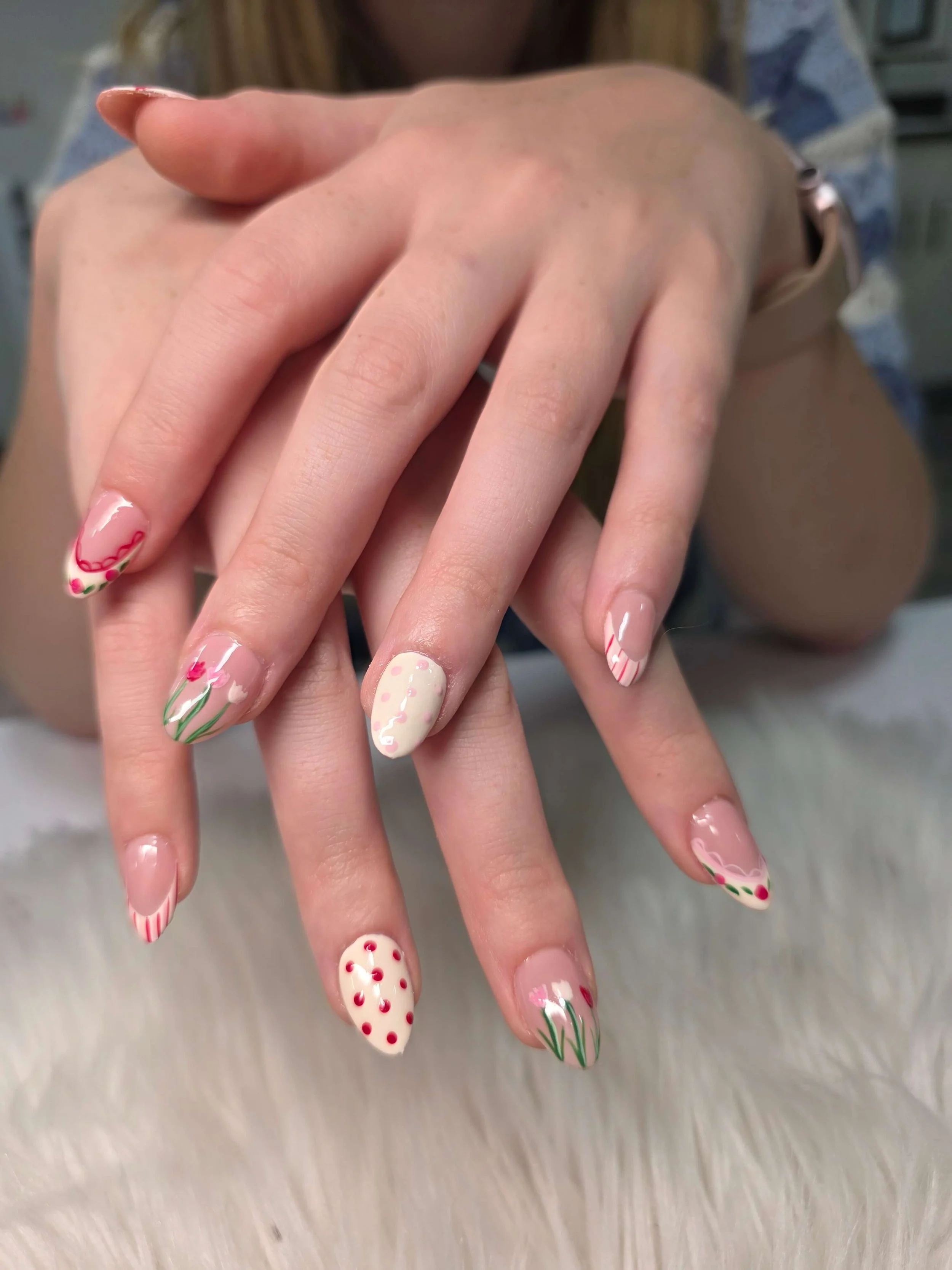 Close-up of hands with decorated nails featuring floral and polka dot patterns in red, pink, and white.