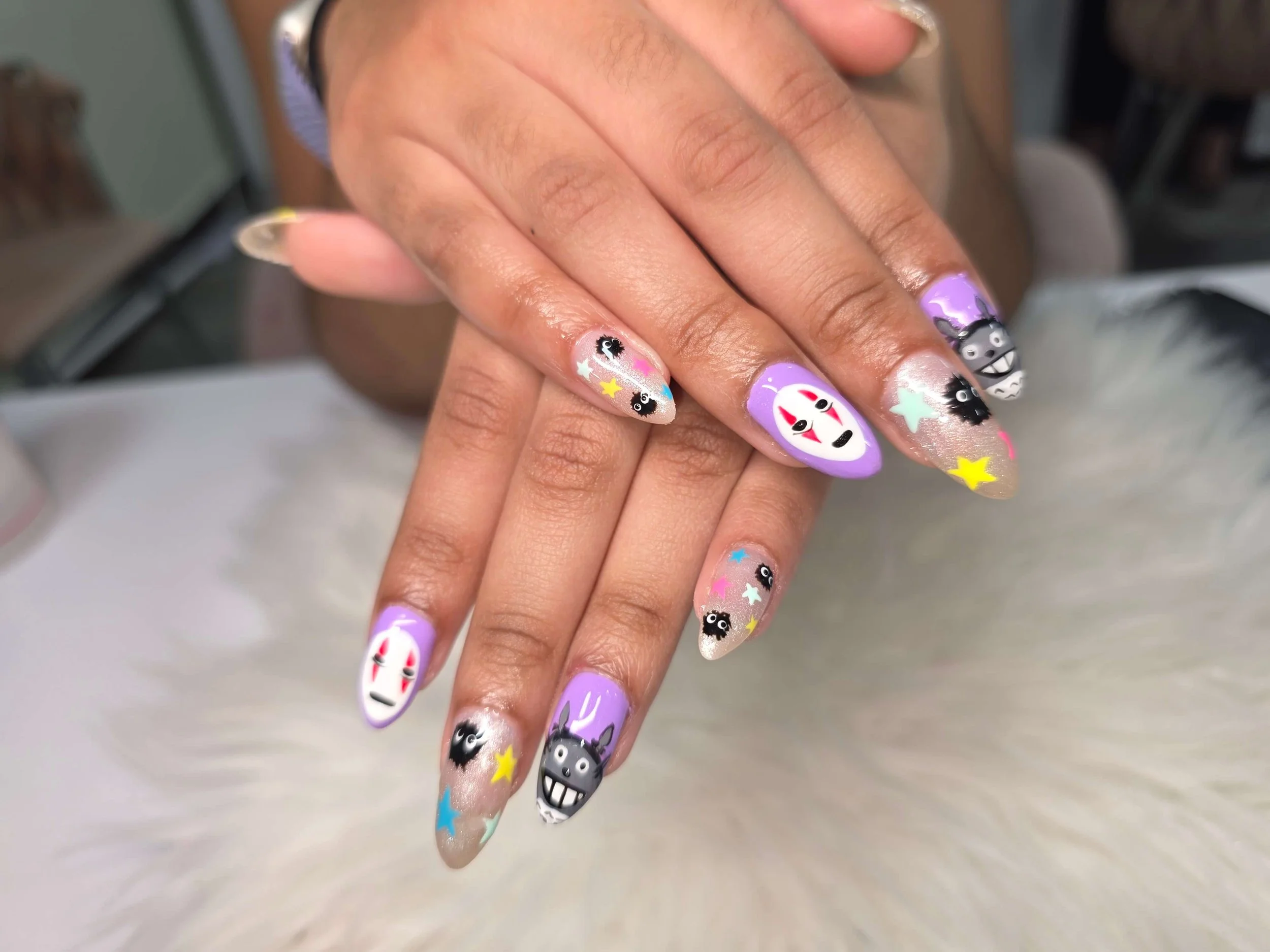 Close-up of a person's hands with colorful, Halloween-themed nail art featuring ghosts, black cats, stars, and other festive designs.