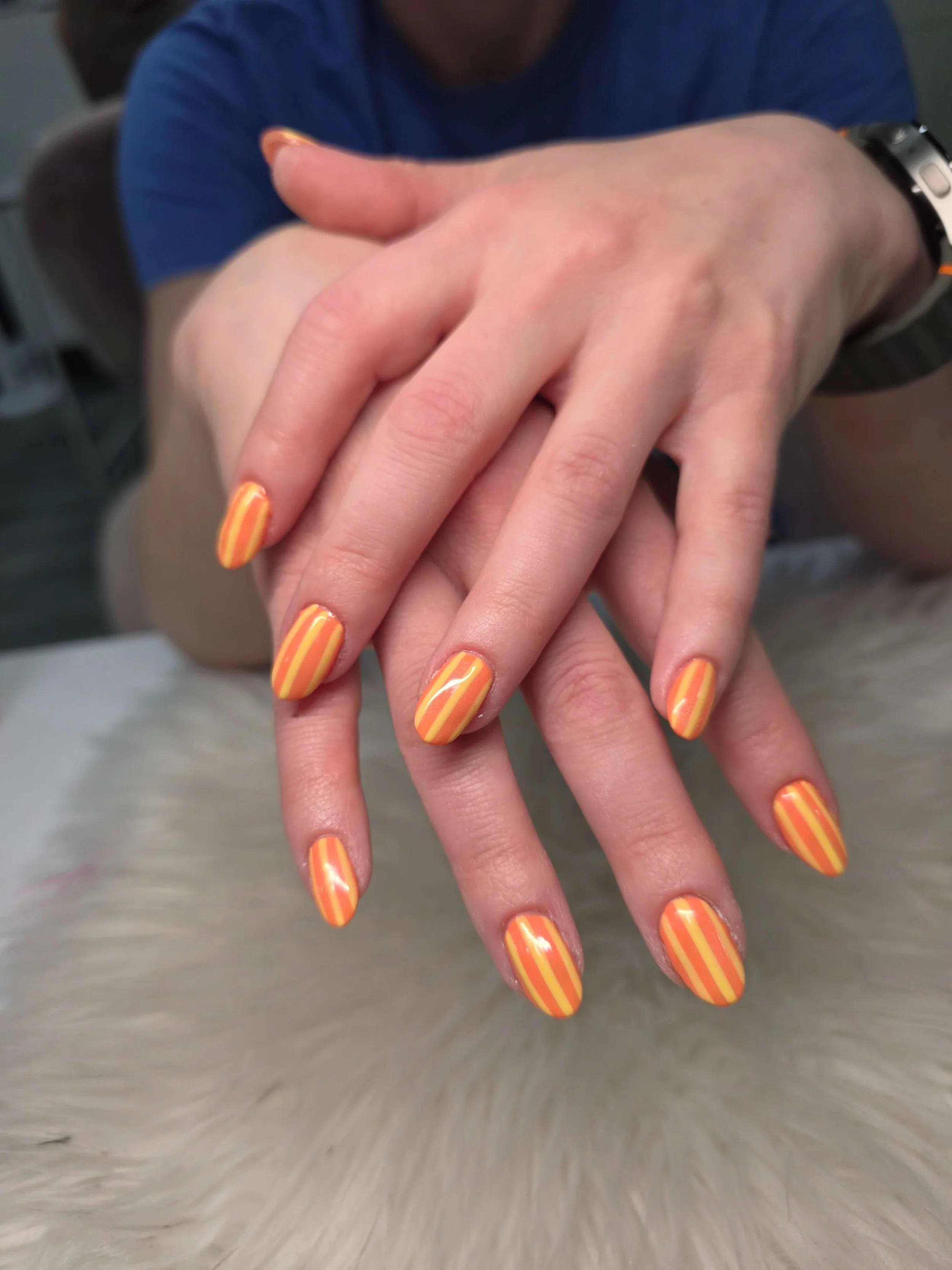 Close-up of a person's hand with orange and yellow striped nail polish, resting on a furry surface.