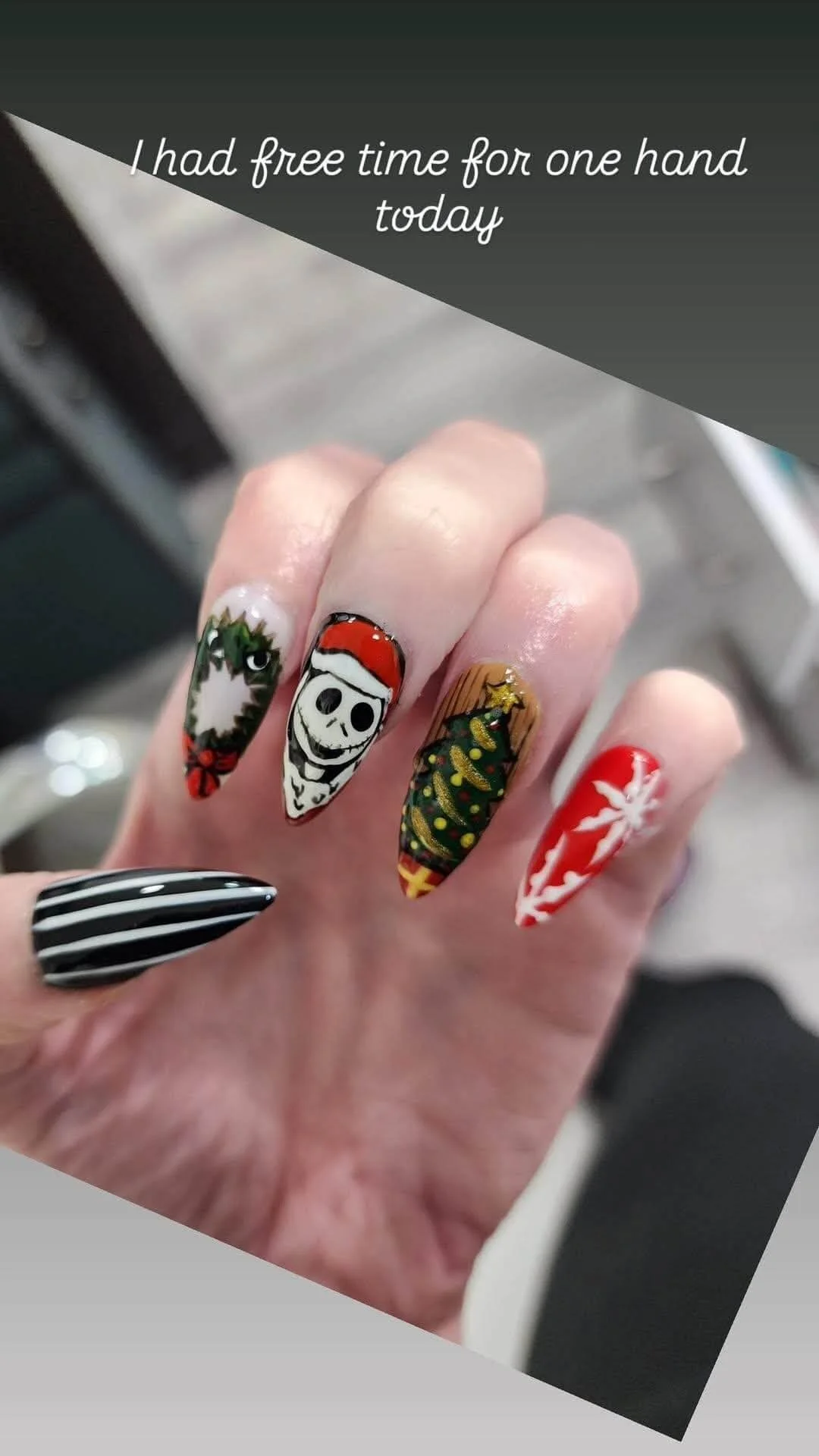 Hand with decorated Christmas-themed nail art, including a snowflake, a Christmas tree, a skull wearing a Santa hat, a striped pattern, and a snowman.