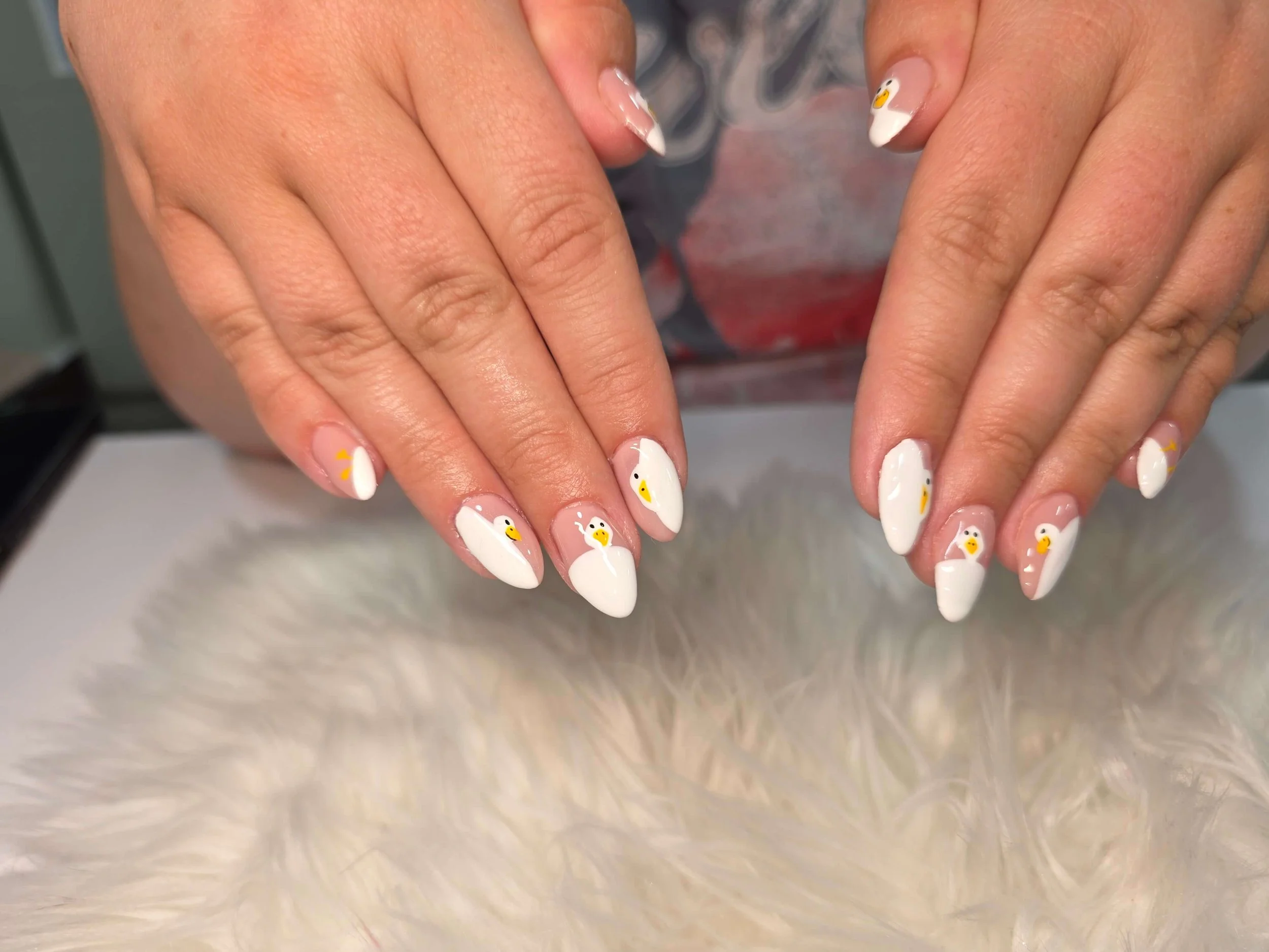 Close-up of hands with white nails adorned with cute duck designs and a fluffy, cream-colored textured background.
