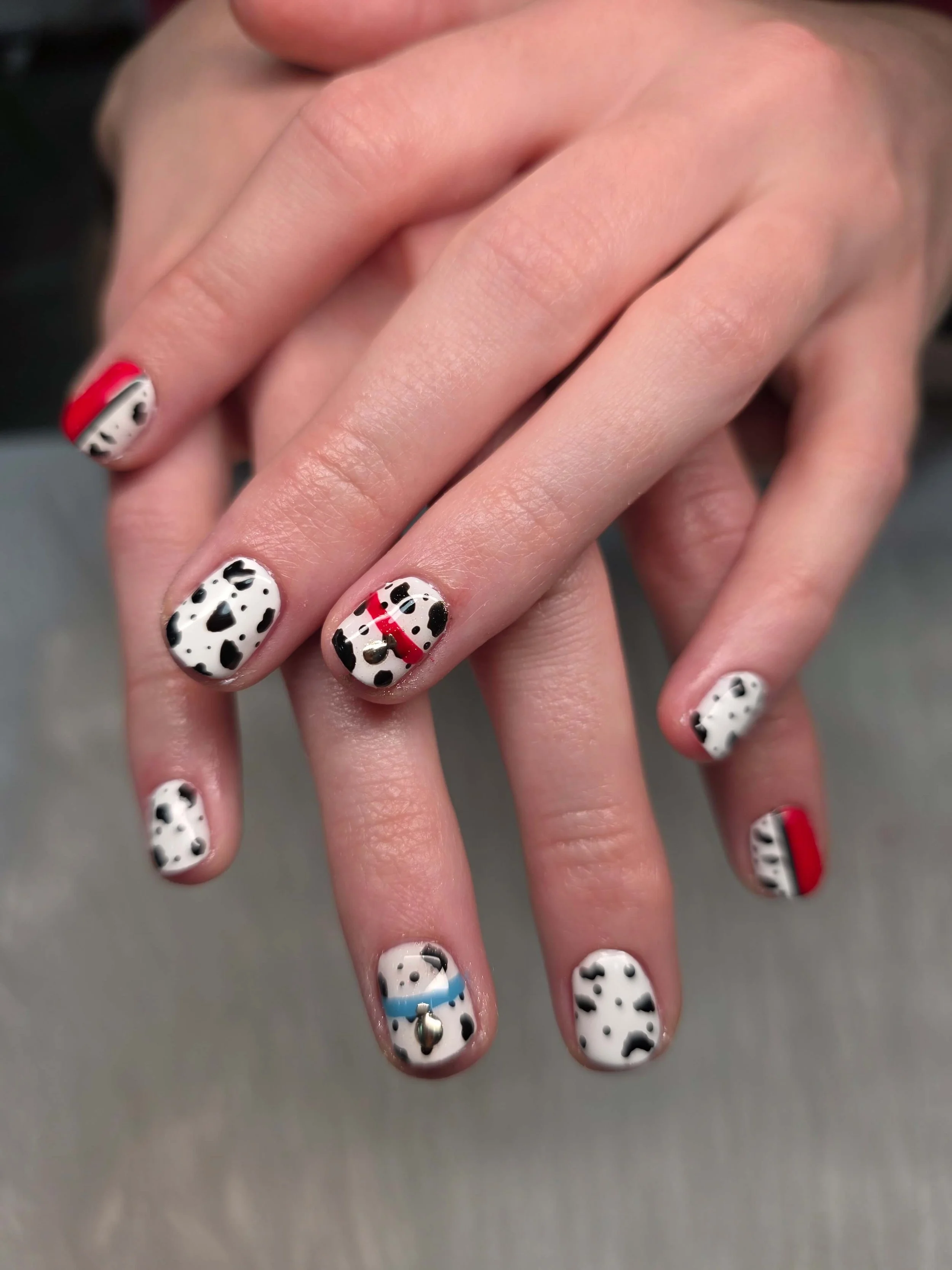 Close-up of manicured fingernails painted with a Dalmatian spot pattern in black and white, with some nails featuring red and blue accents.