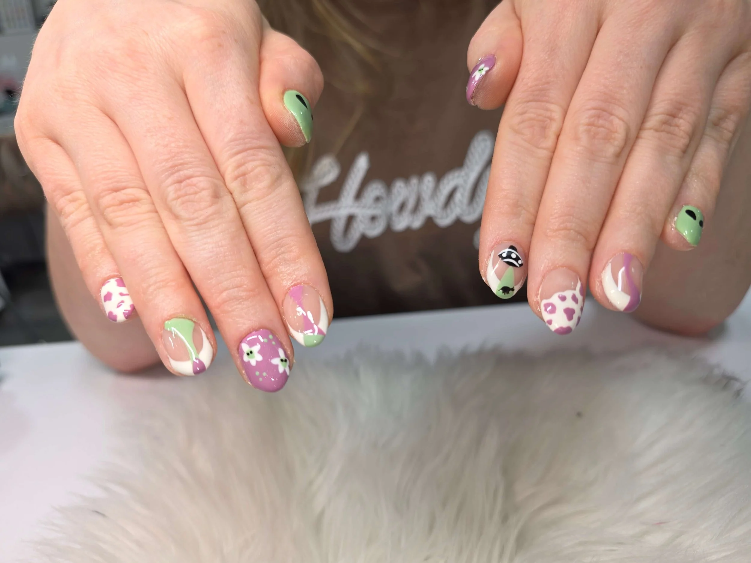 Close-up of a person's hands showing colorful nail art with various designs, including flowers, animal prints, and abstract patterns.