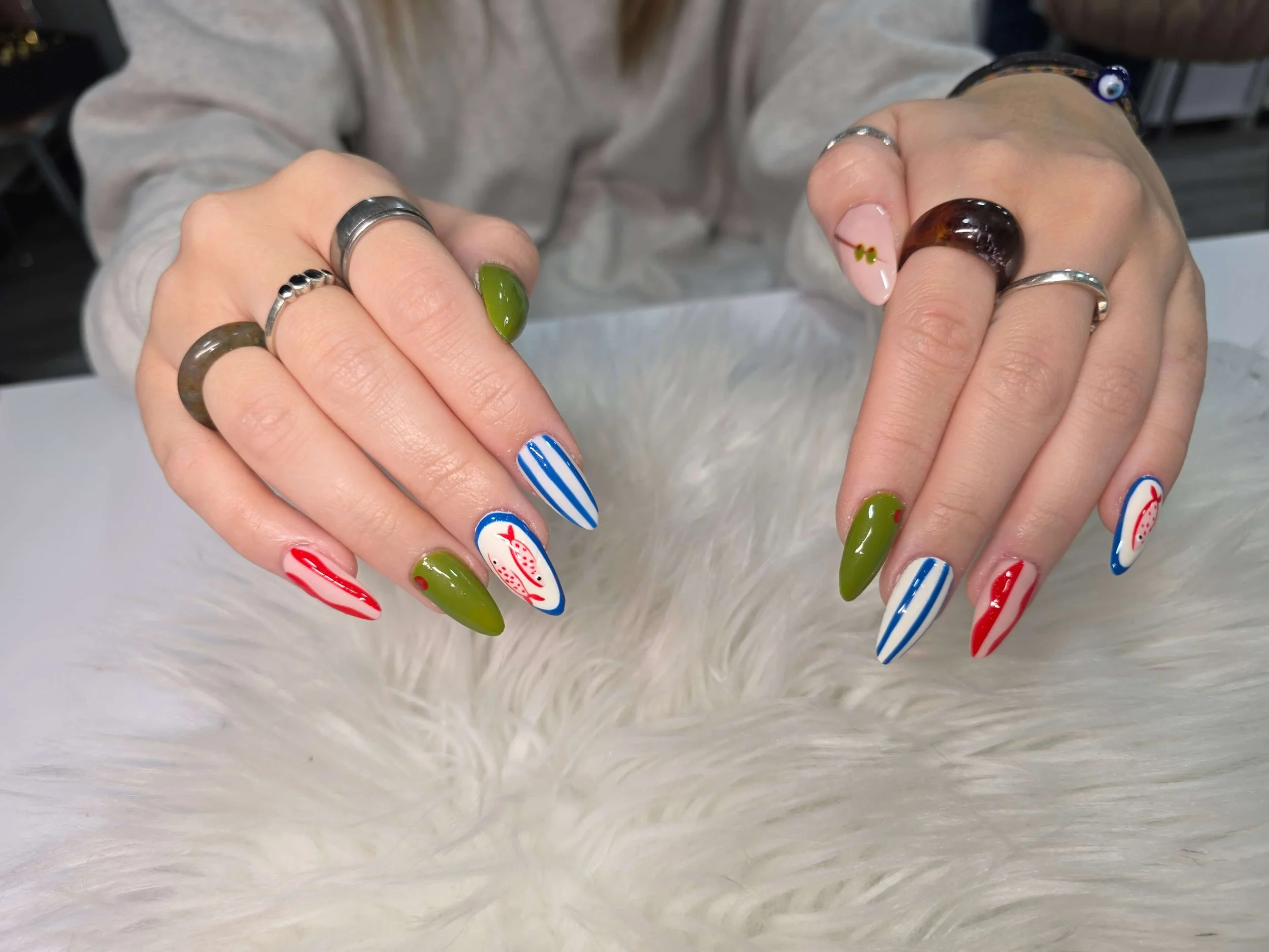 Close-up of hands displaying colorful holiday-themed nail art and silver rings, resting on a white furry surface.