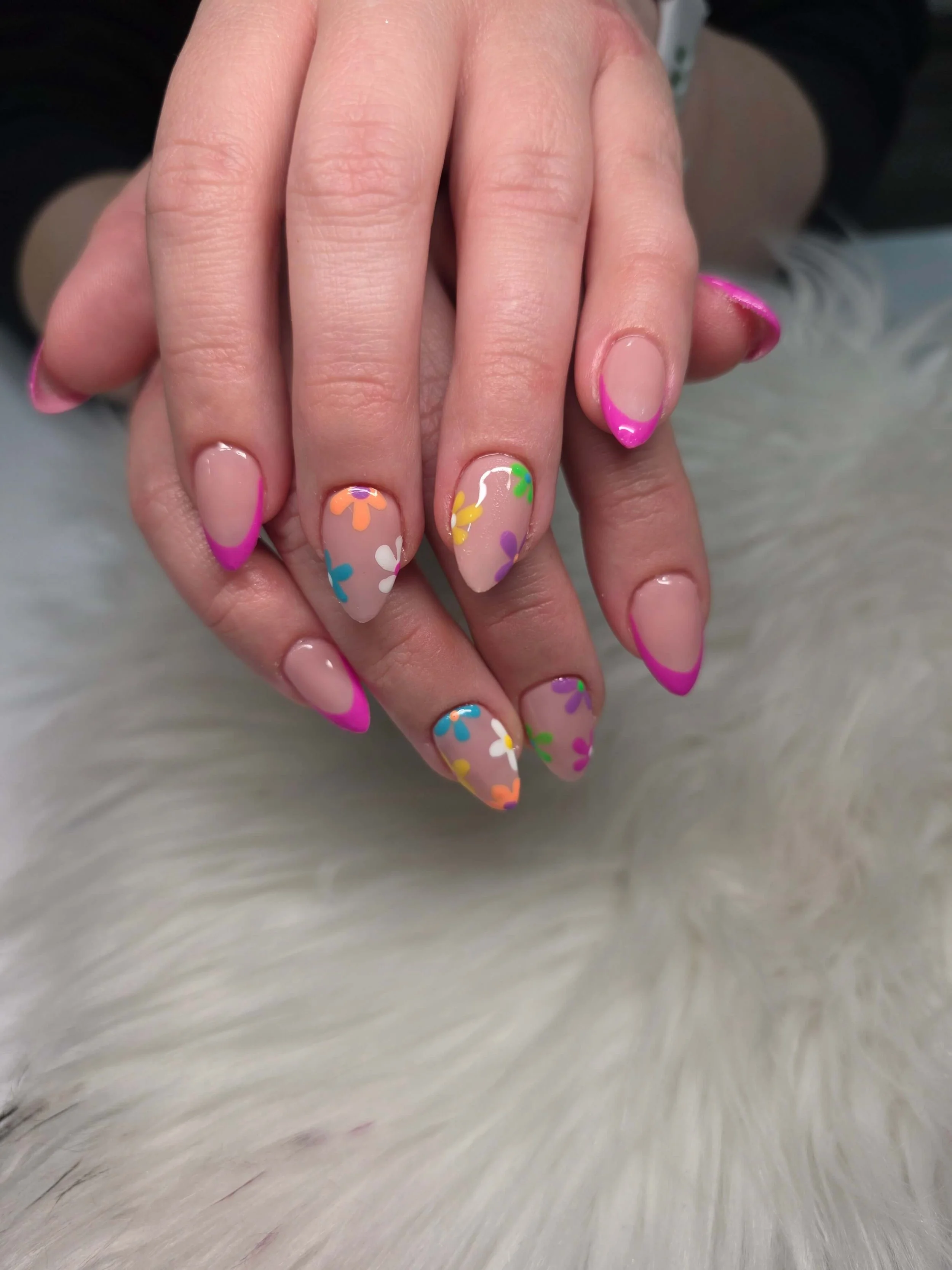 Close-up of two hands with colorful floral nail art, including pink French tips and multicolored flower designs on the nails.