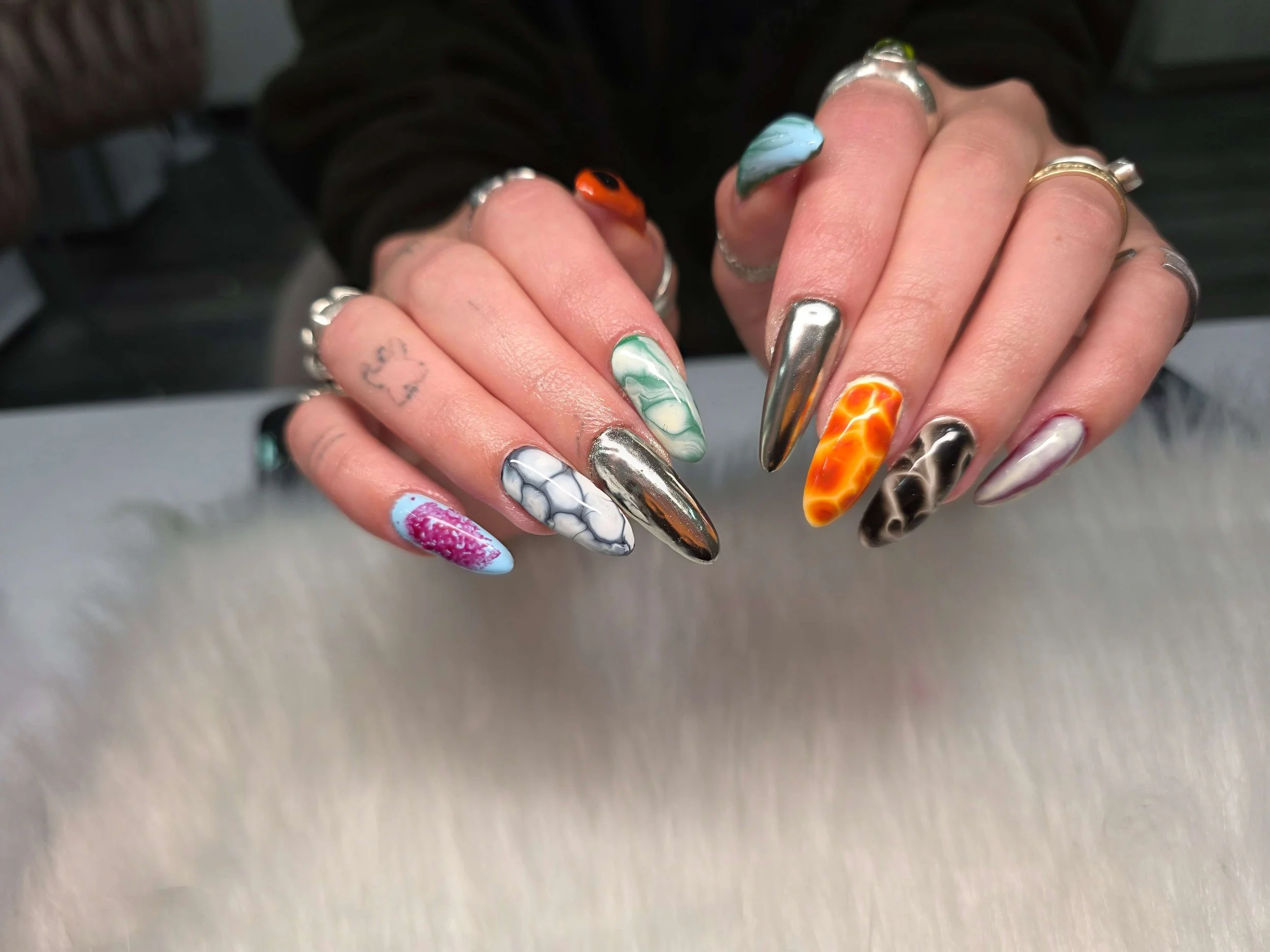 Close-up of a person's hand with colorful, elaborate, and artistic nail designs, featuring various patterns and shades.