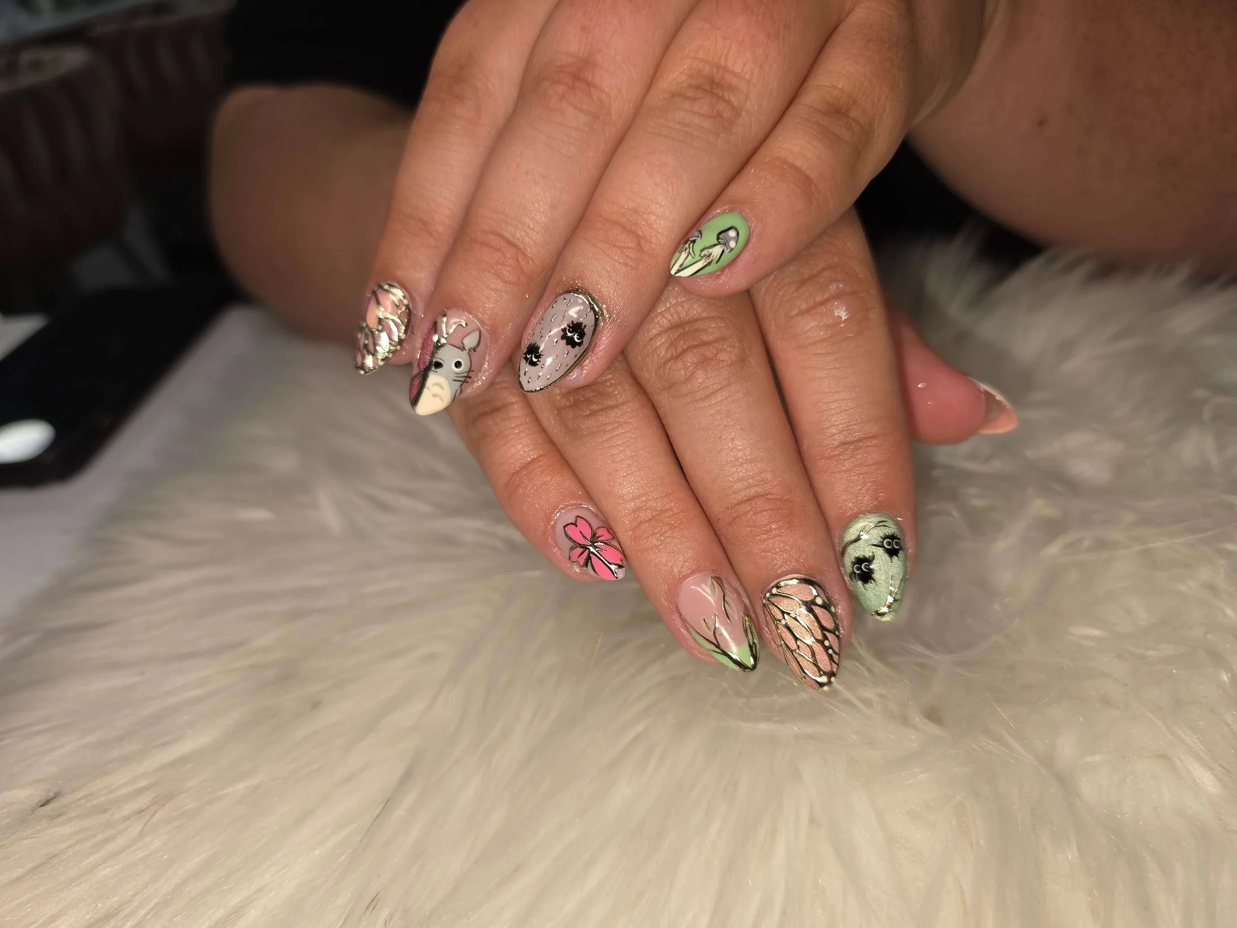 Close-up of a person's hand with decorated fingernails featuring various colorful and patterned nail art designs, resting on a white furry surface.