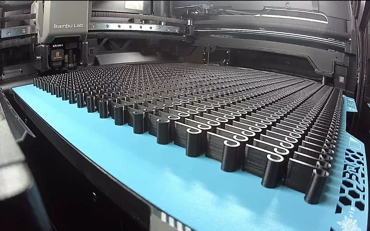 Close-up of a Bambu Lab 3D printer printing black filament on a blue print bed.