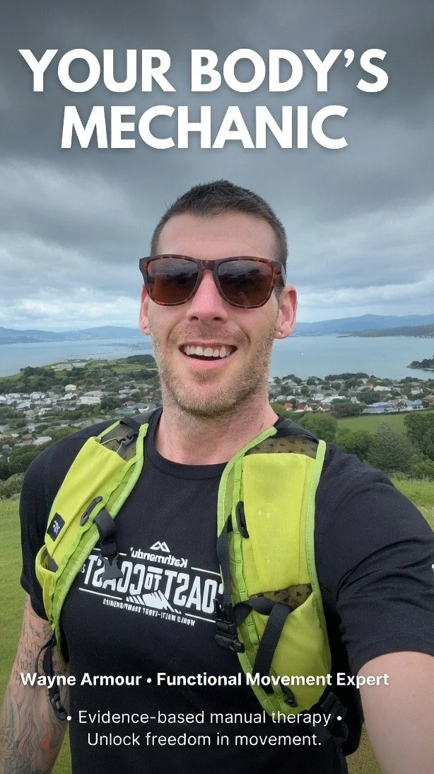 A smiling man wearing sunglasses and a black t-shirt with white text, carrying a bright yellow backpack, outdoors near a body of water with hills and a town in the background. The image has text that says, "Your body's mechanic," and mentions Wayne Armour as a functional movement expert specializing in evidence-based manual therapy and unlocking freedom in movement.