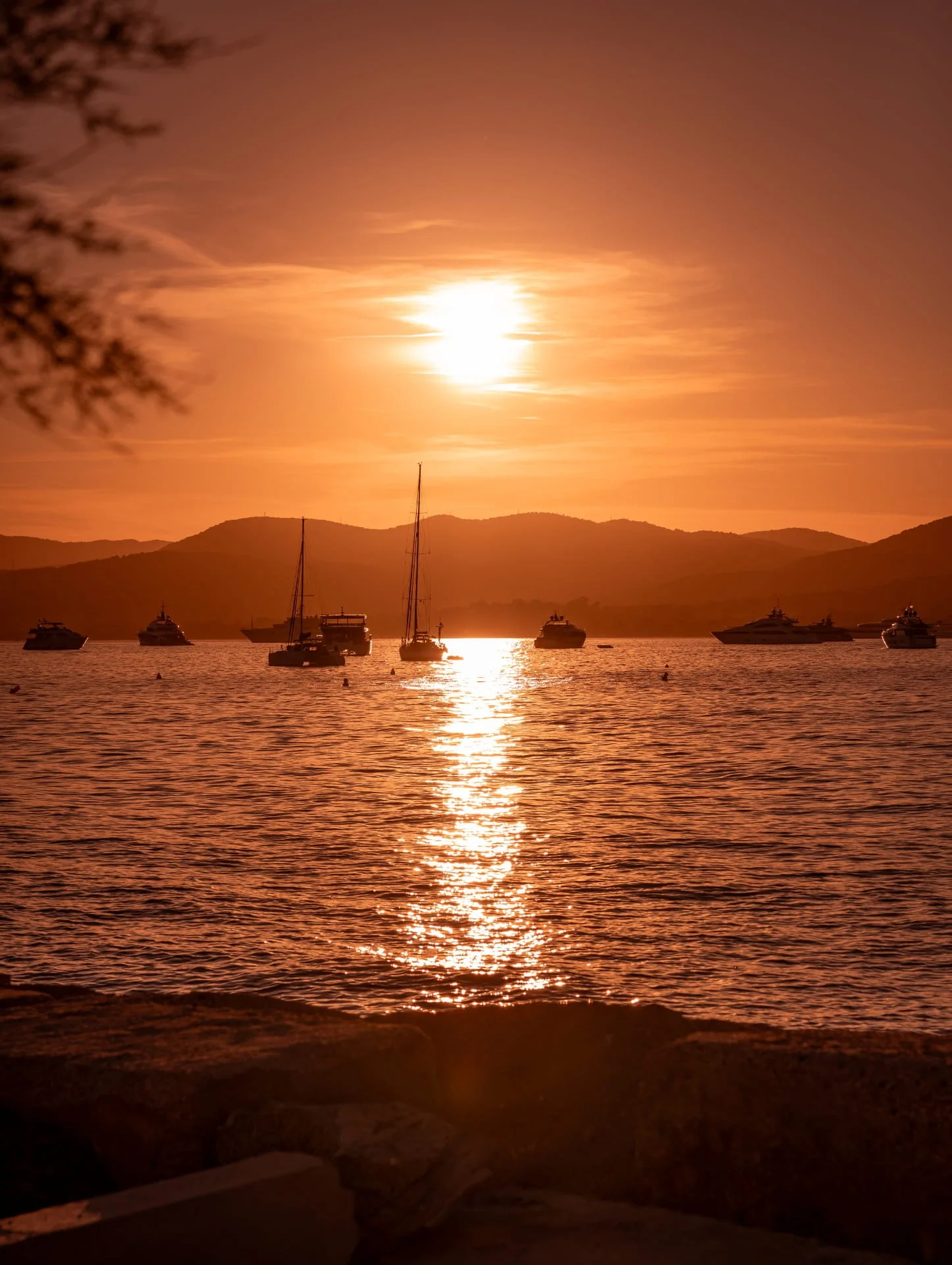 Sunset over a body of water with boats and mountains in the background.