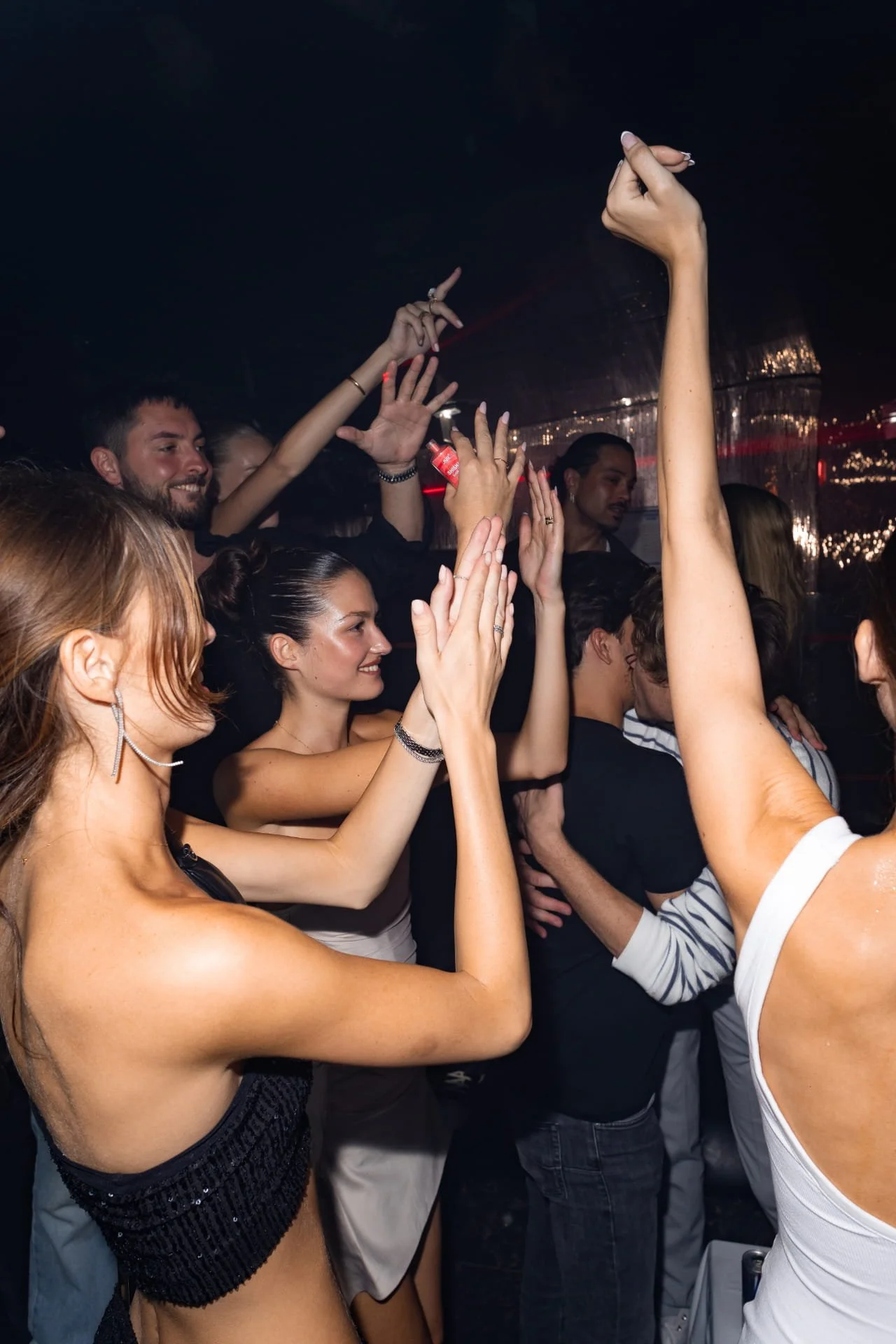 People dancing and enjoying themselves at a nightclub or party venue with dark lighting and reflections on the walls.