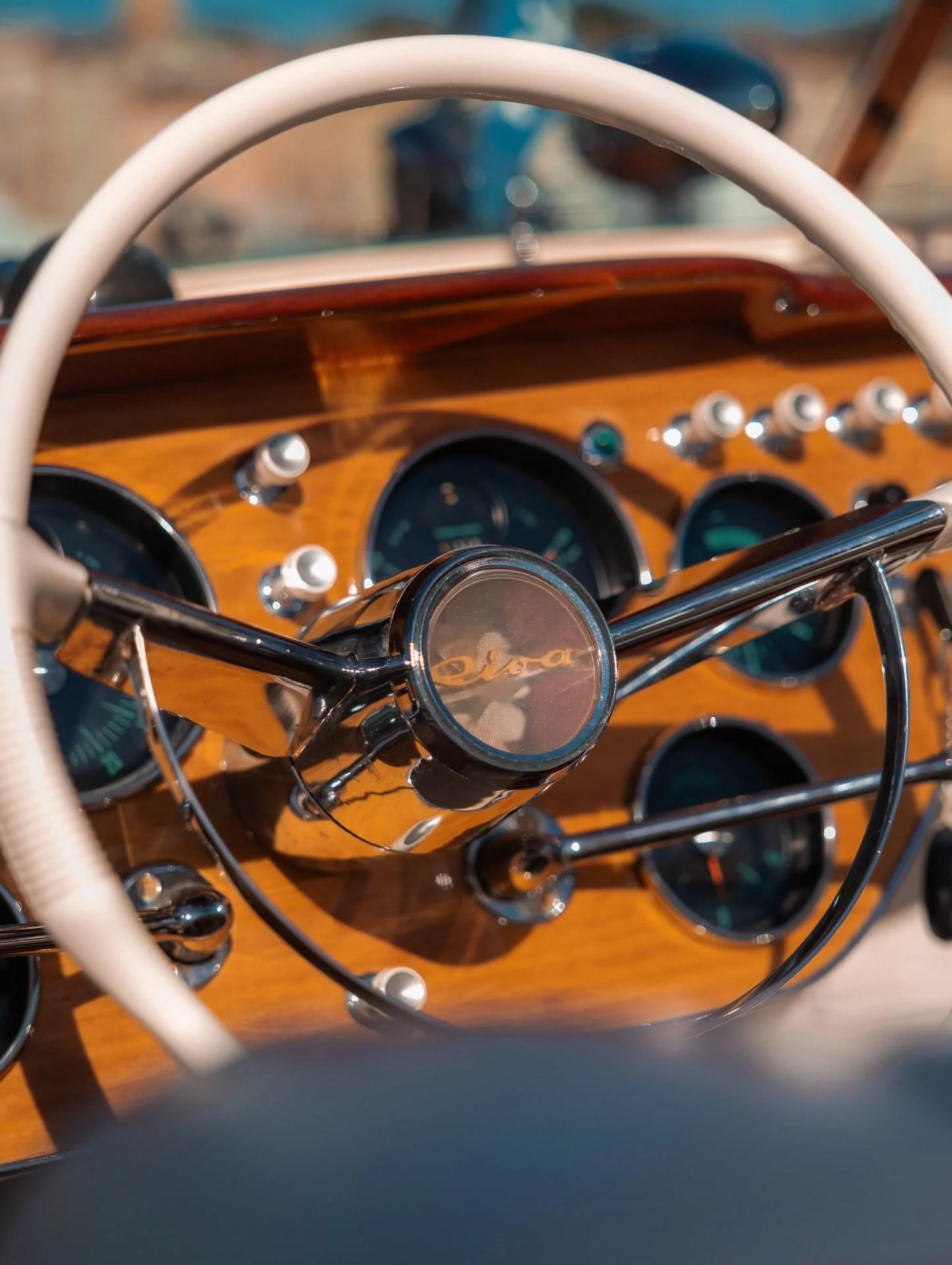 Close-up of a vintage car dashboard with a wooden panel, several gauges, and chrome accents, viewed through the steering wheel.