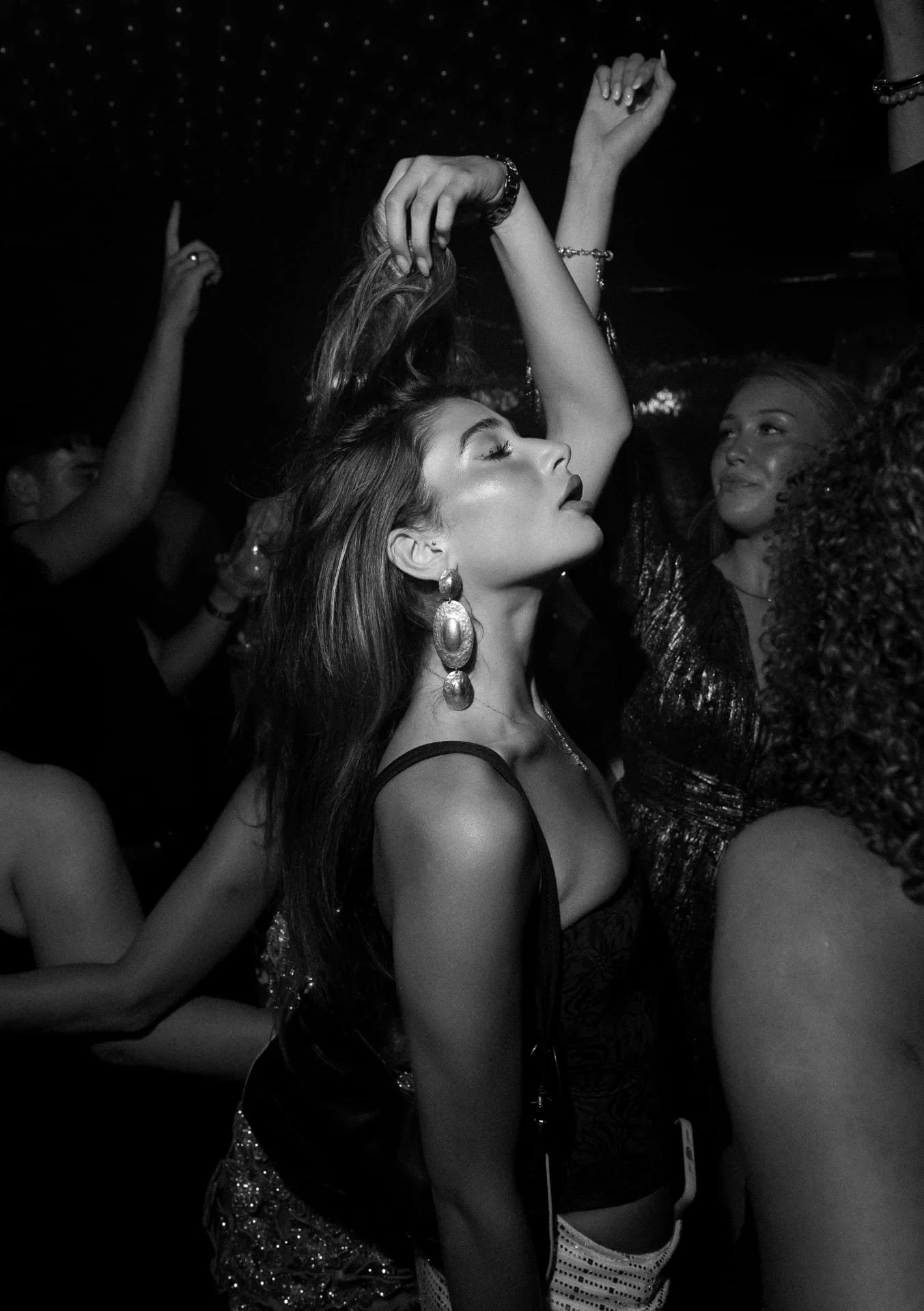 Women dancing at a party or club, some wearing shimmering outfits and jewelry, with their eyes closed or gazing serenely, enjoying the music and atmosphere.