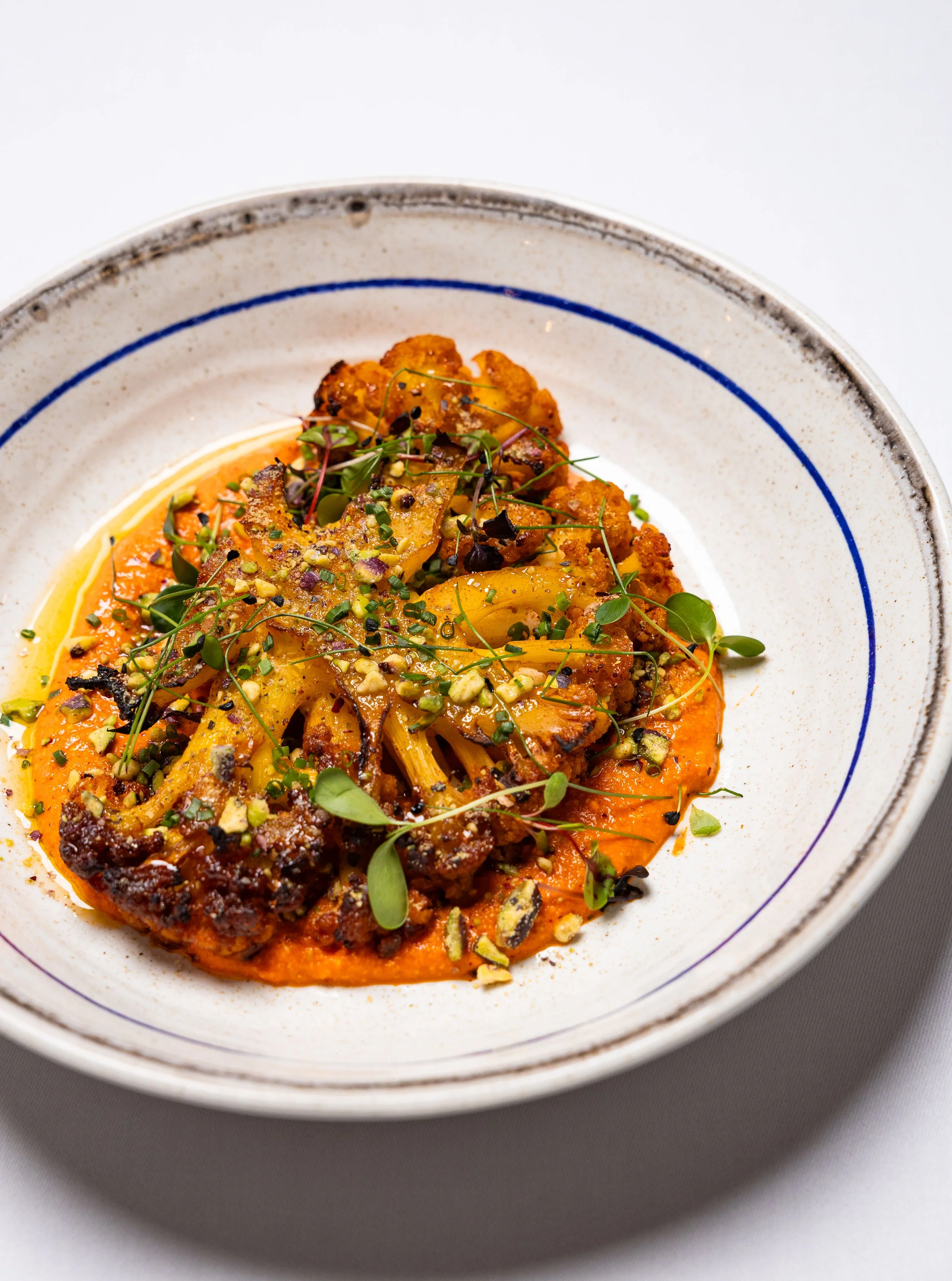 A bowl of pasta topped with herbs, nuts, and a sauce, garnished with microgreens.