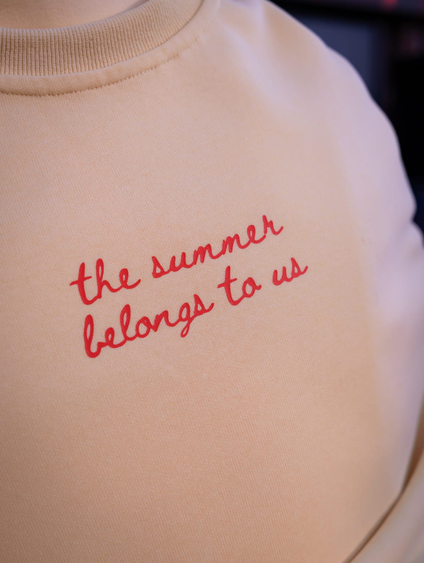 Close-up of a pinkish-beige shirt with red cursive text reading 'the summer was to u'.