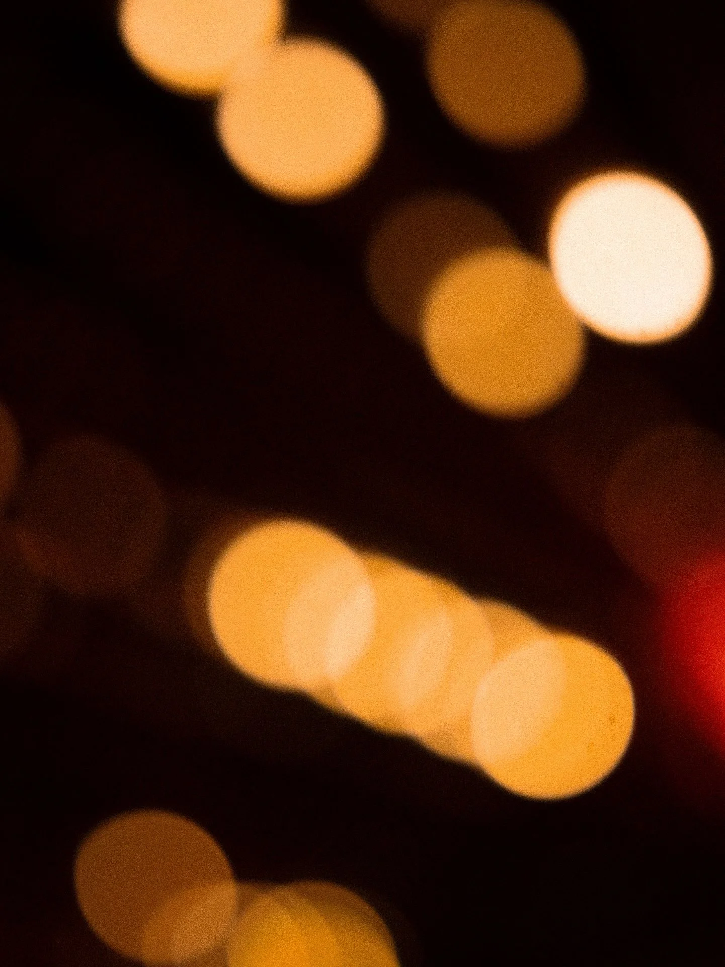 Blurred image of warm yellow and orange bokeh lights against a dark background.