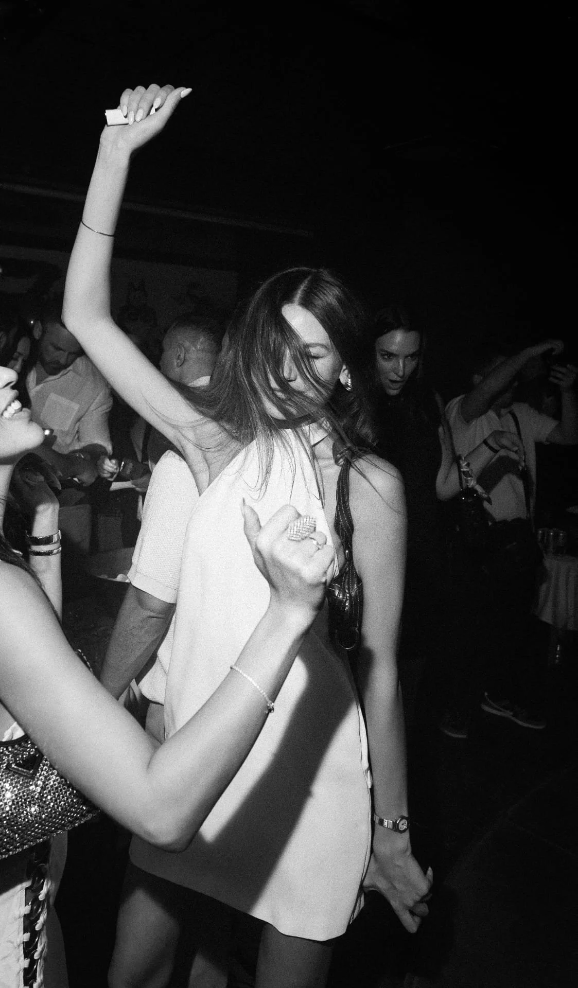 Women dancing and enjoying themselves at a party or nightclub, with one woman in the center with shoulder-length hair, closed eyes, and a big smile.
