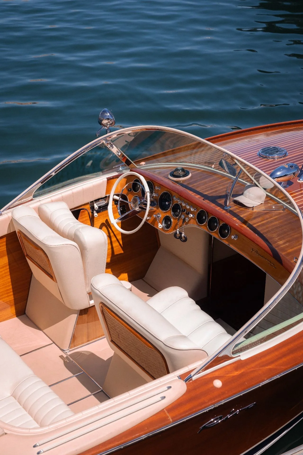 Close-up of a luxury boat interior with white leather seats, a wood-paneled dashboard, and a clear windshield, floating on water.