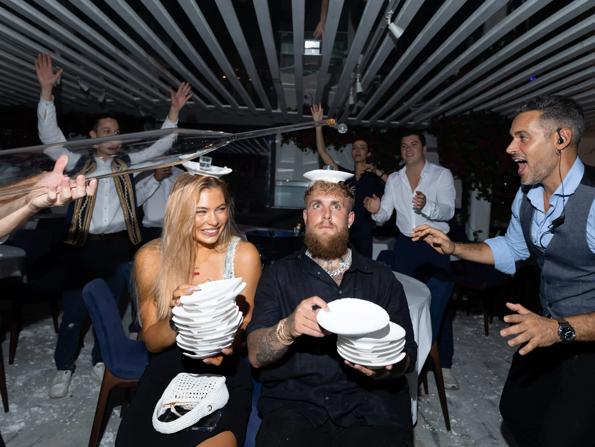 People celebrating at a party with a waiter balancing a tray of stacked plates.