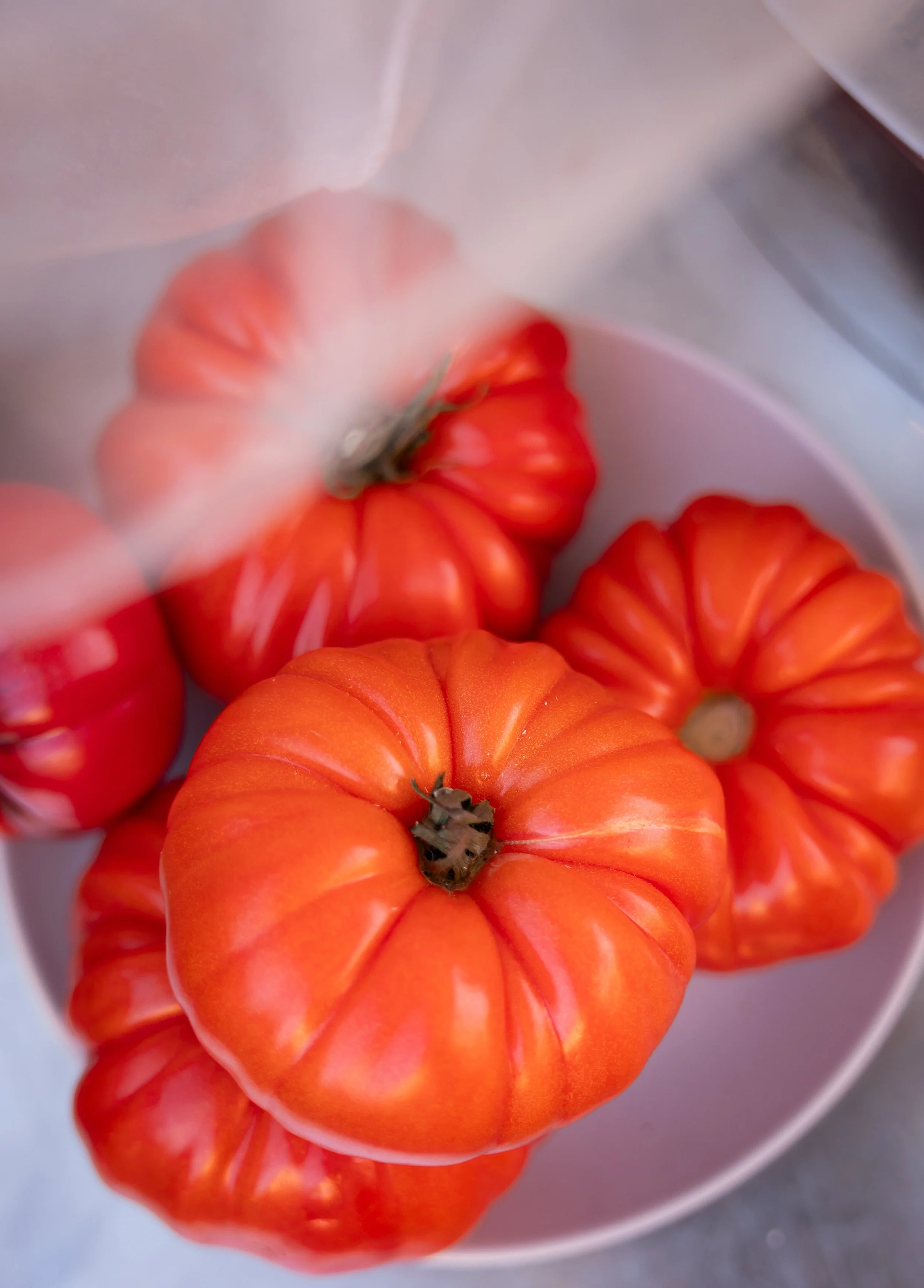 Multiple small orange tomatoes with ridges, displayed in a white bowl.