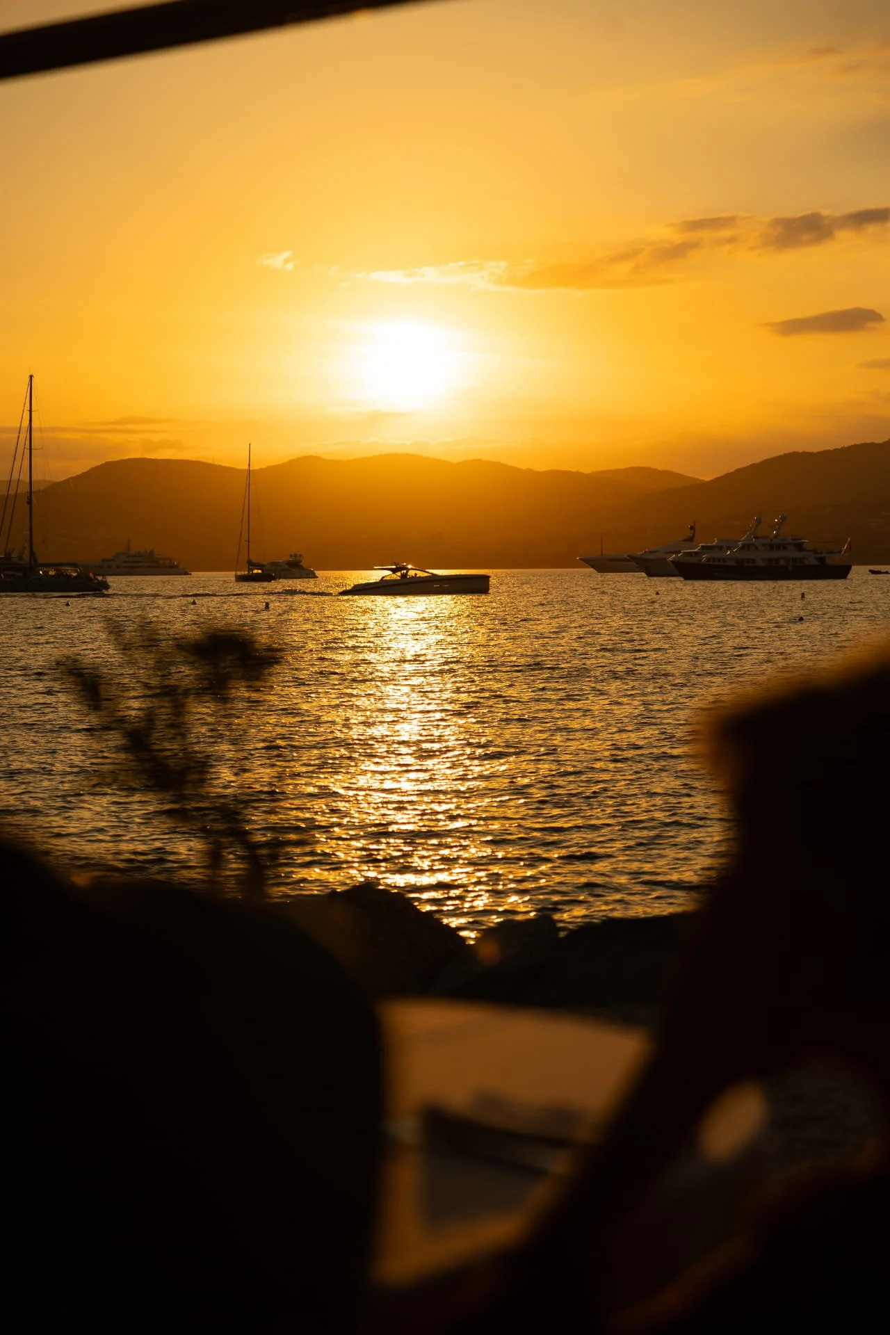Sunset over mountains with boats on a calm body of water.