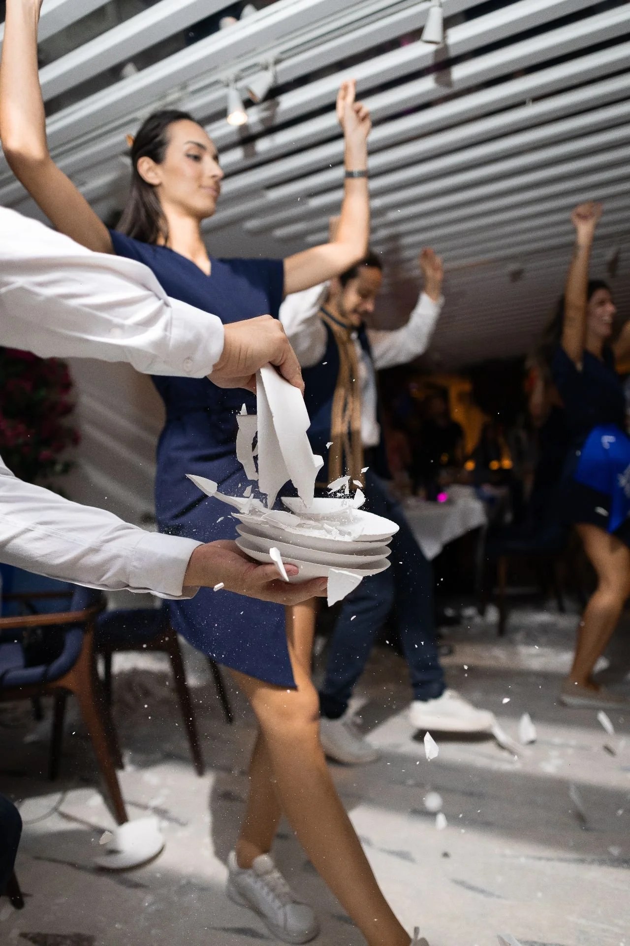People participating in a pie-throwing event, one person caught in mid-air with a pie breaking on a plate, others with raised hands, in an indoor setting.