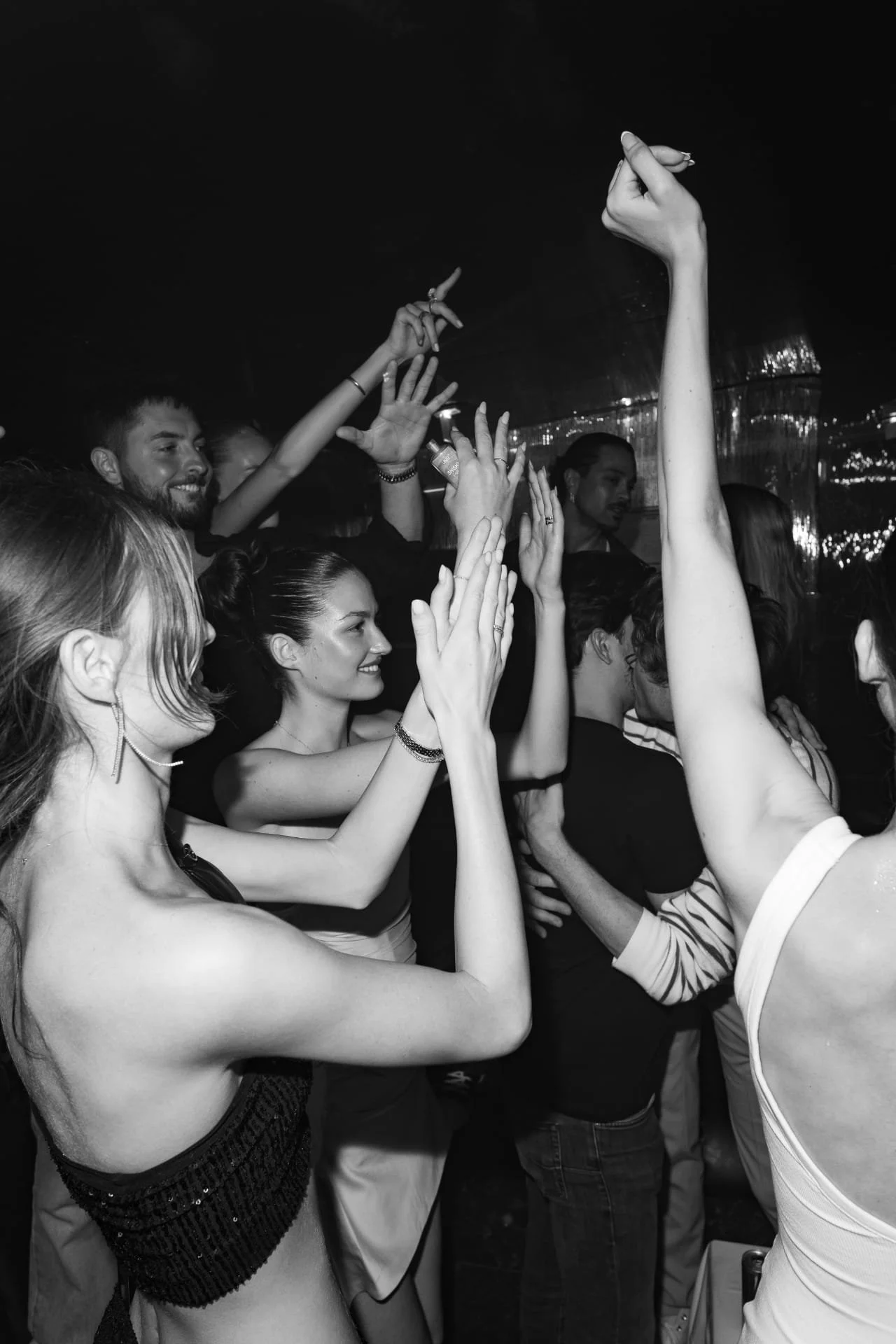A group of people dancing and raising their hands at a party or nightclub, captured in black and white.
