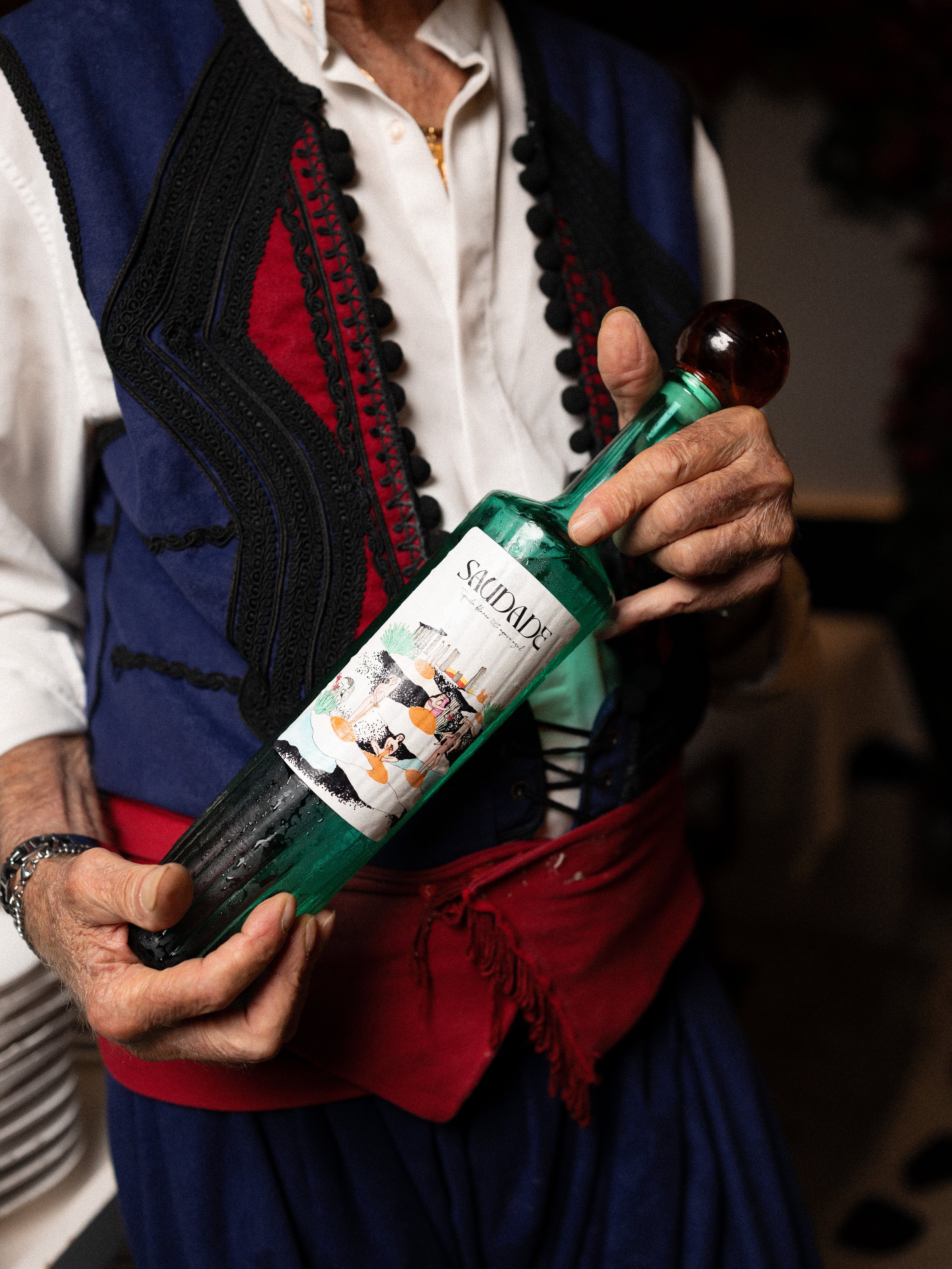 A person holding a bottle of sparkling water with a colorful label, wearing a traditional embroidered jacket and a white shirt.