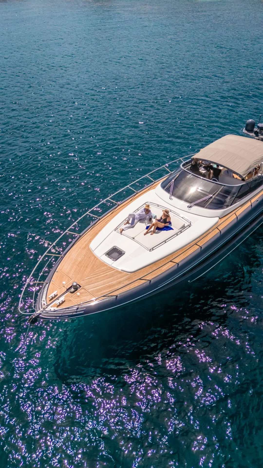 Two people relaxing on the sun deck of a yacht, floating on calm blue water.