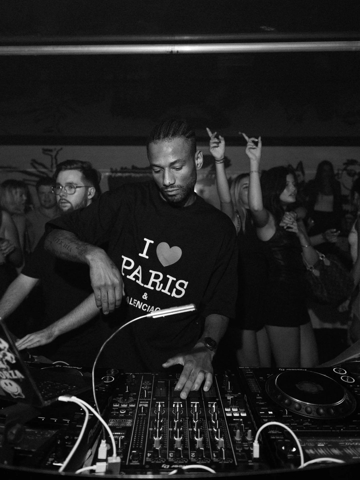 Black and white photo of a man DJing at a party, surrounded by a crowd of people dancing and enjoying music.