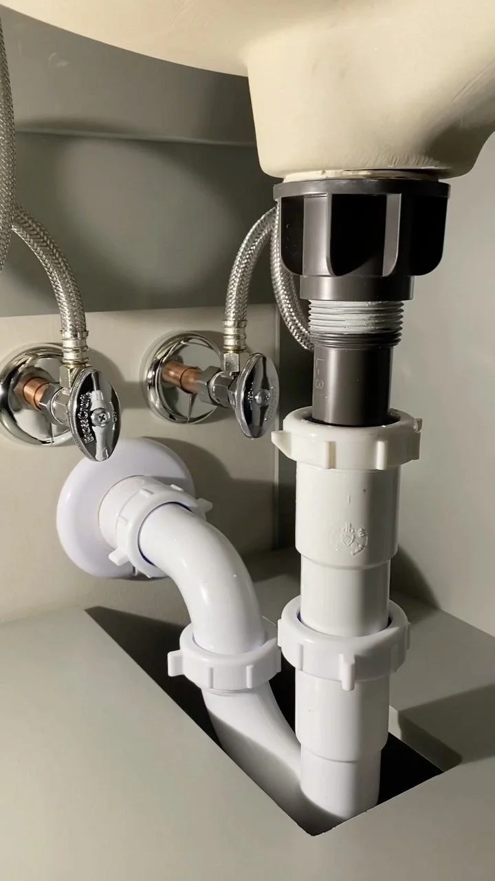 Under sink plumbing with PVC pipes and shut-off valves.