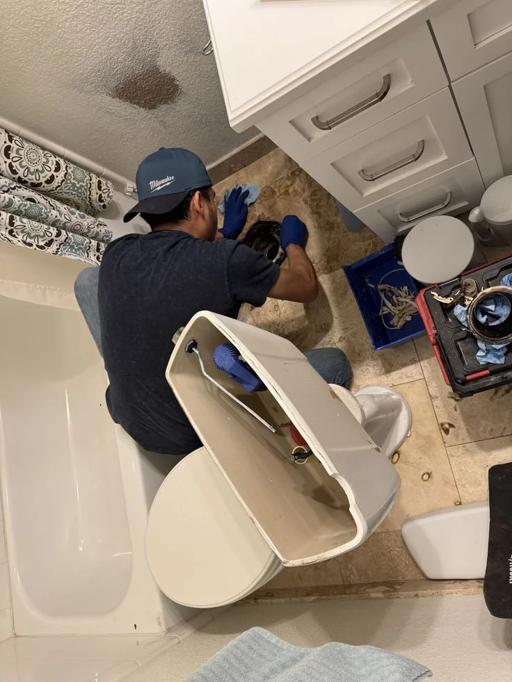 Man working on bathroom toilet, with the tank lid removed and tools nearby.